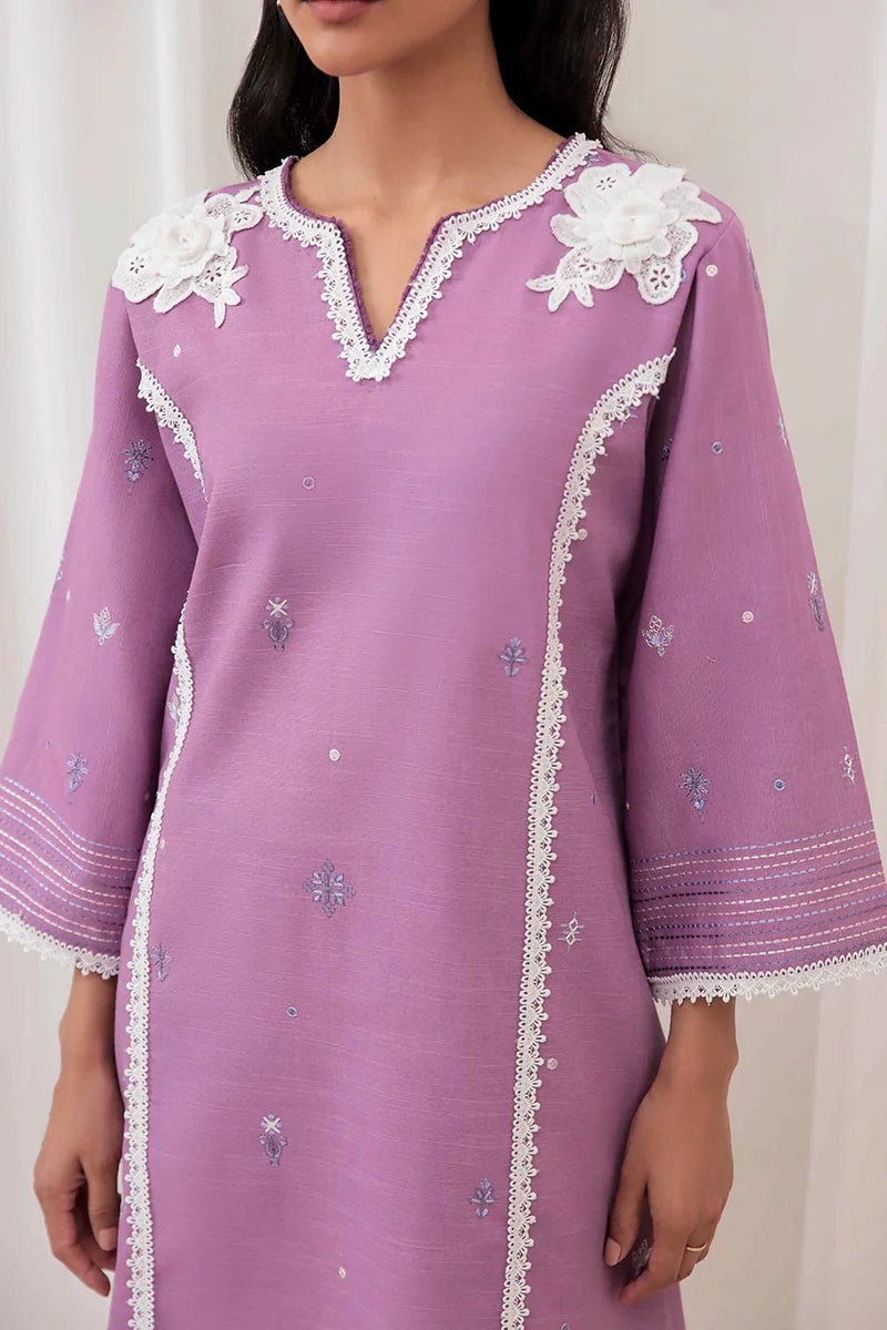 Model wearing Mushq Wisteria Winter Basic Pret '24 Frost Flair, a lavender dress adorned with white lace details, perfect for winter casual wear. Available for Pakistani clothes online in the UK.