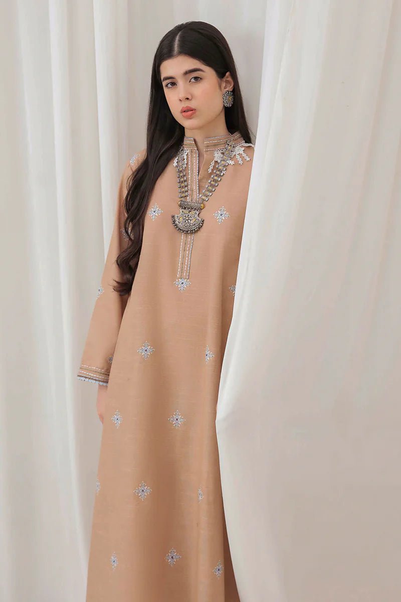 Model wearing Mushq Wisteria Winter Basic Pret '24 Frost Kissed, a beige dress with subtle blue embroidery, ideal for winter casual wear. Available for Pakistani clothes online in the UK.