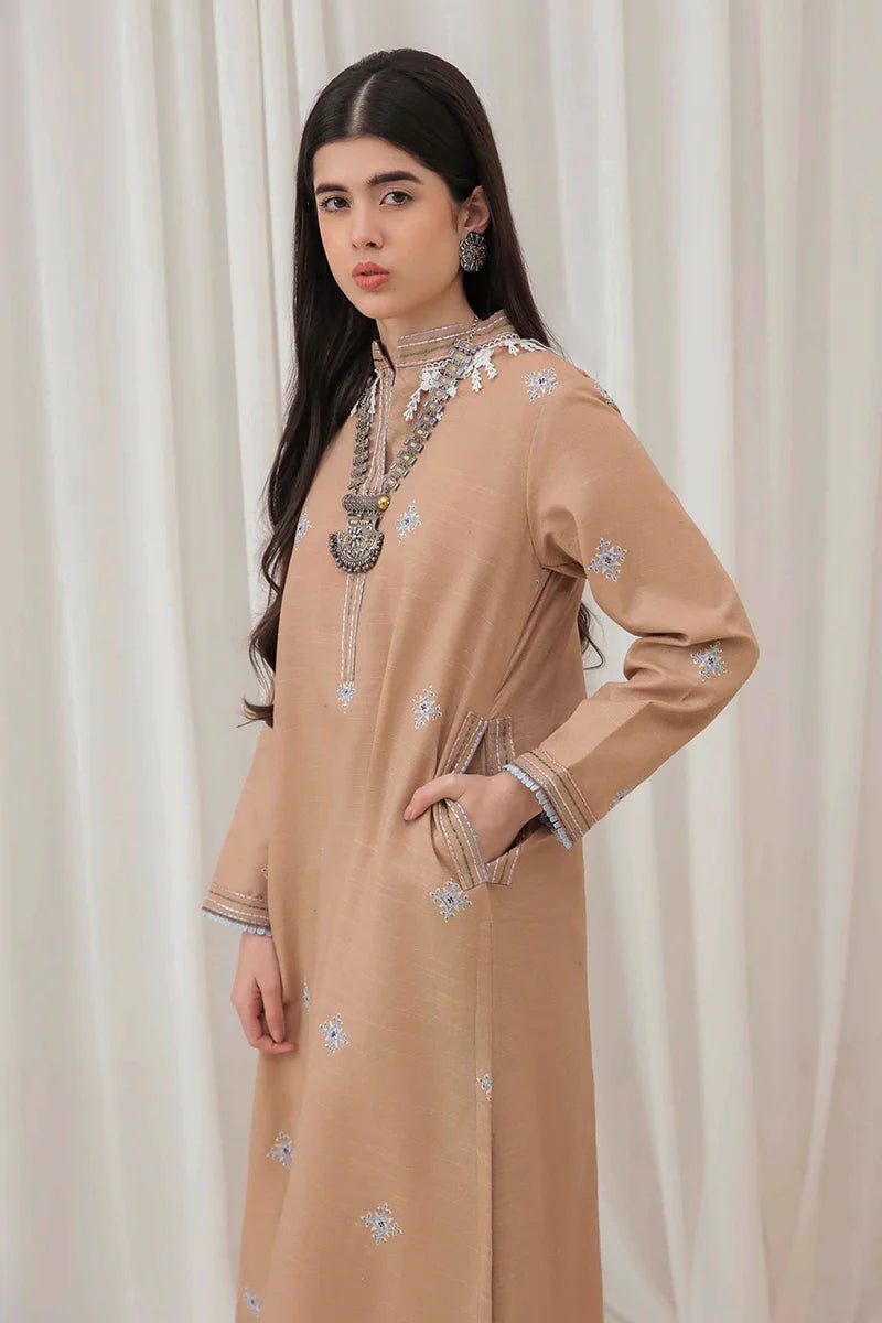 Model wearing Mushq Wisteria Winter Basic Pret '24 Frost Kissed, a beige dress with subtle blue embroidery, ideal for winter casual wear. Available for Pakistani clothes online in the UK.