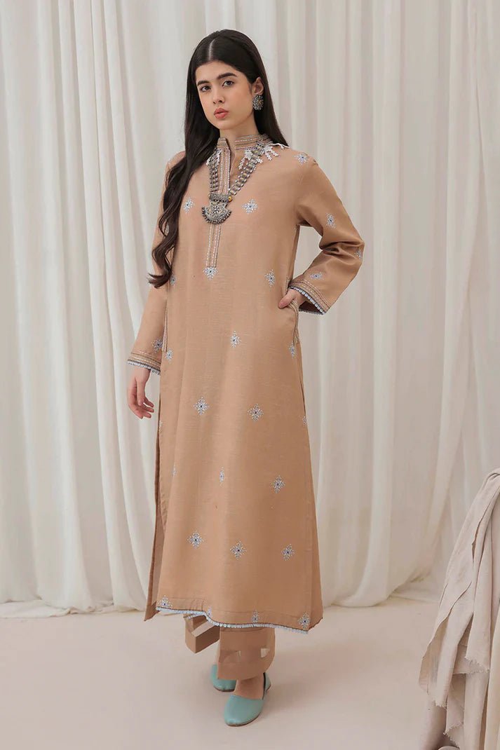 Model wearing Mushq Wisteria Winter Basic Pret '24 Frost Kissed, a beige dress with subtle blue embroidery, ideal for winter casual wear. Available for Pakistani clothes online in the UK.