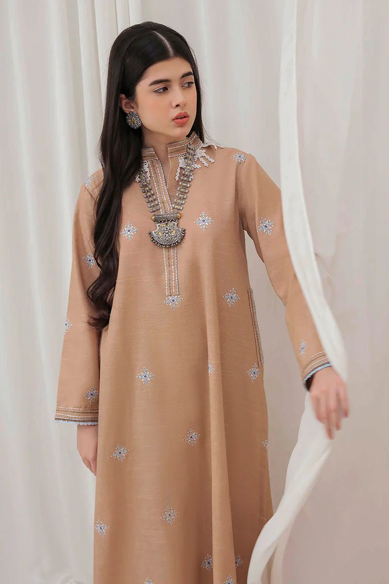 Model wearing Mushq Wisteria Winter Basic Pret '24 Frost Kissed, a beige dress with subtle blue embroidery, ideal for winter casual wear. Available for Pakistani clothes online in the UK.