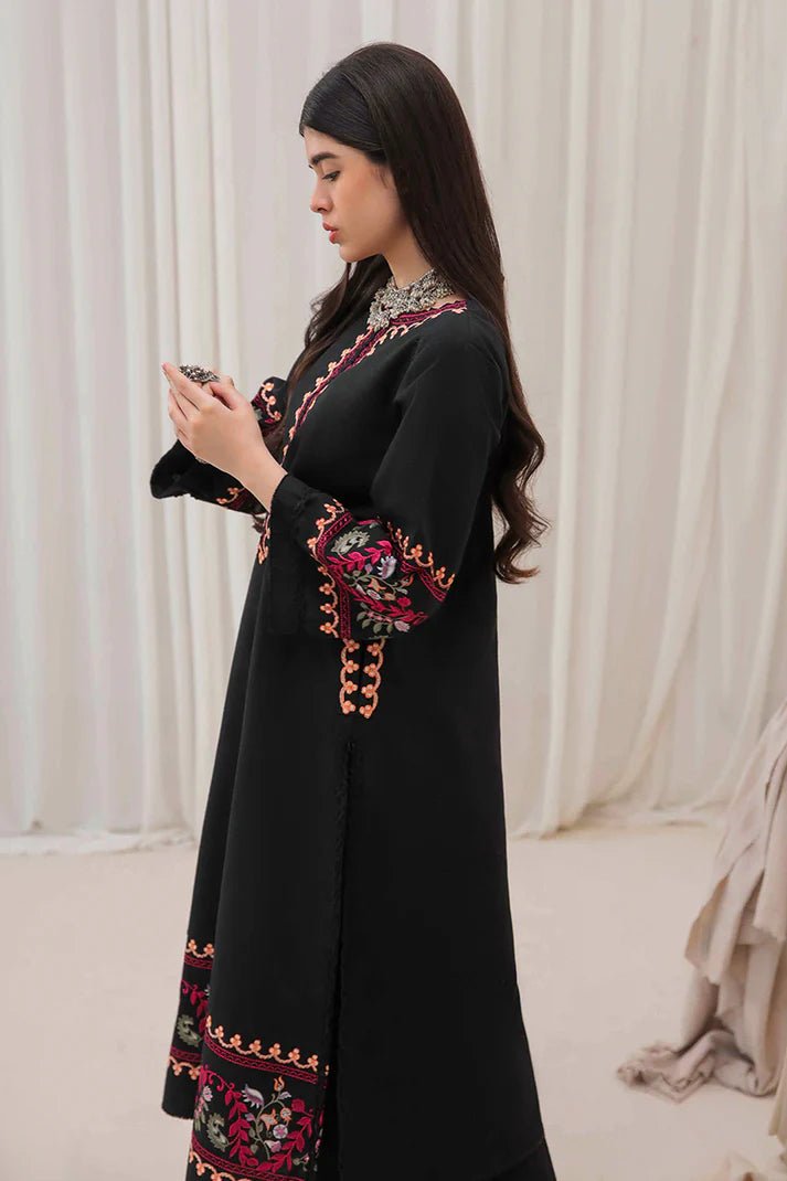 Model wearing Mushq Wisteria Winter Basic Pret '24 Whispering Winds, a black dress with vibrant floral embroidery, ideal for winter casual wear. Available for Pakistani clothes online in the UK.