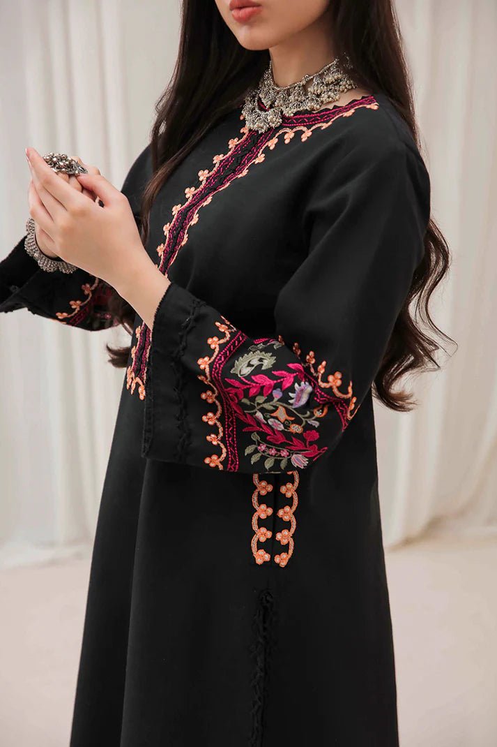 Model wearing Mushq Wisteria Winter Basic Pret '24 Whispering Winds, a black dress with vibrant floral embroidery, ideal for winter casual wear. Available for Pakistani clothes online in the UK.