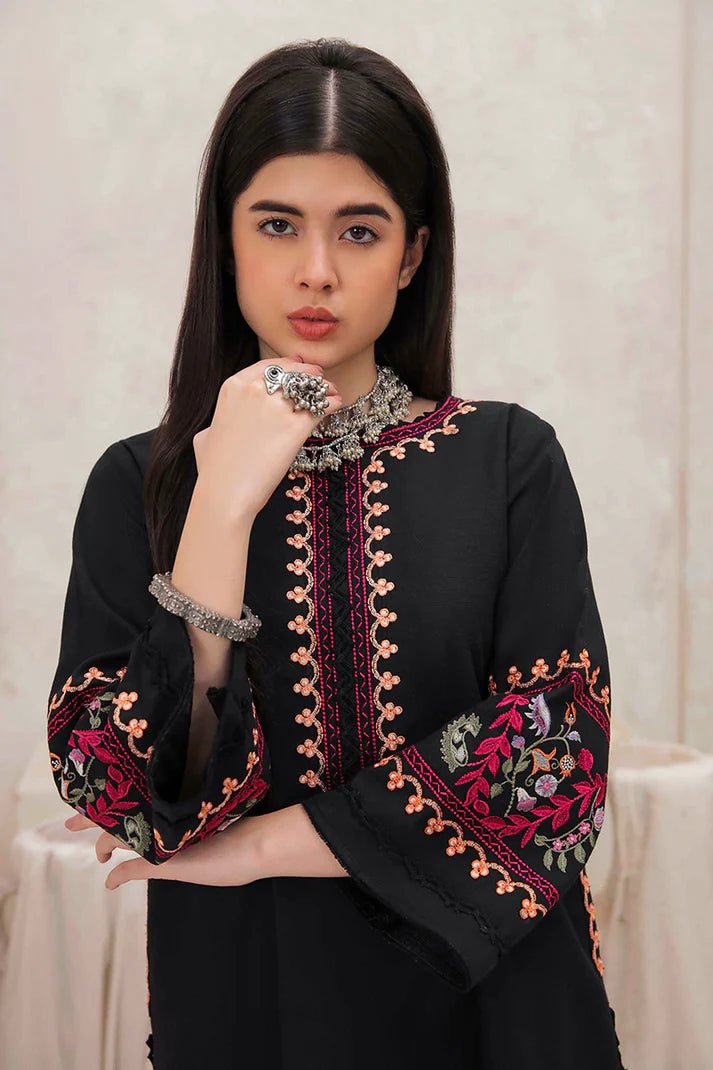 Model wearing Mushq Wisteria Winter Basic Pret '24 Whispering Winds, a black dress with vibrant floral embroidery, ideal for winter casual wear. Available for Pakistani clothes online in the UK.