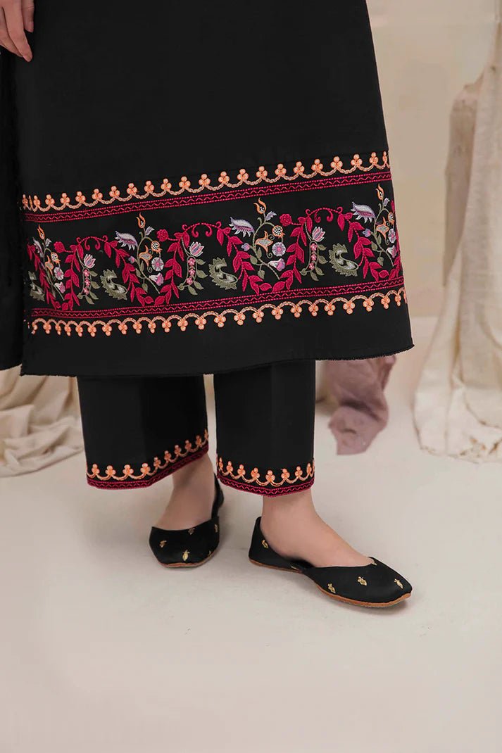 Model wearing Mushq Wisteria Winter Basic Pret '24 Whispering Winds, a black dress with vibrant floral embroidery, ideal for winter casual wear. Available for Pakistani clothes online in the UK.