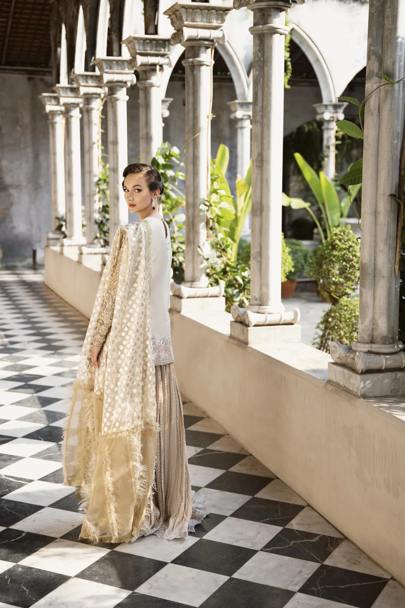 Model wearing a gold and red embellished GLEAM dress from Mysie by Tahira. Perfect for weddings, showcasing intricate embroidery. Shop Pakistani clothes online in the UK.