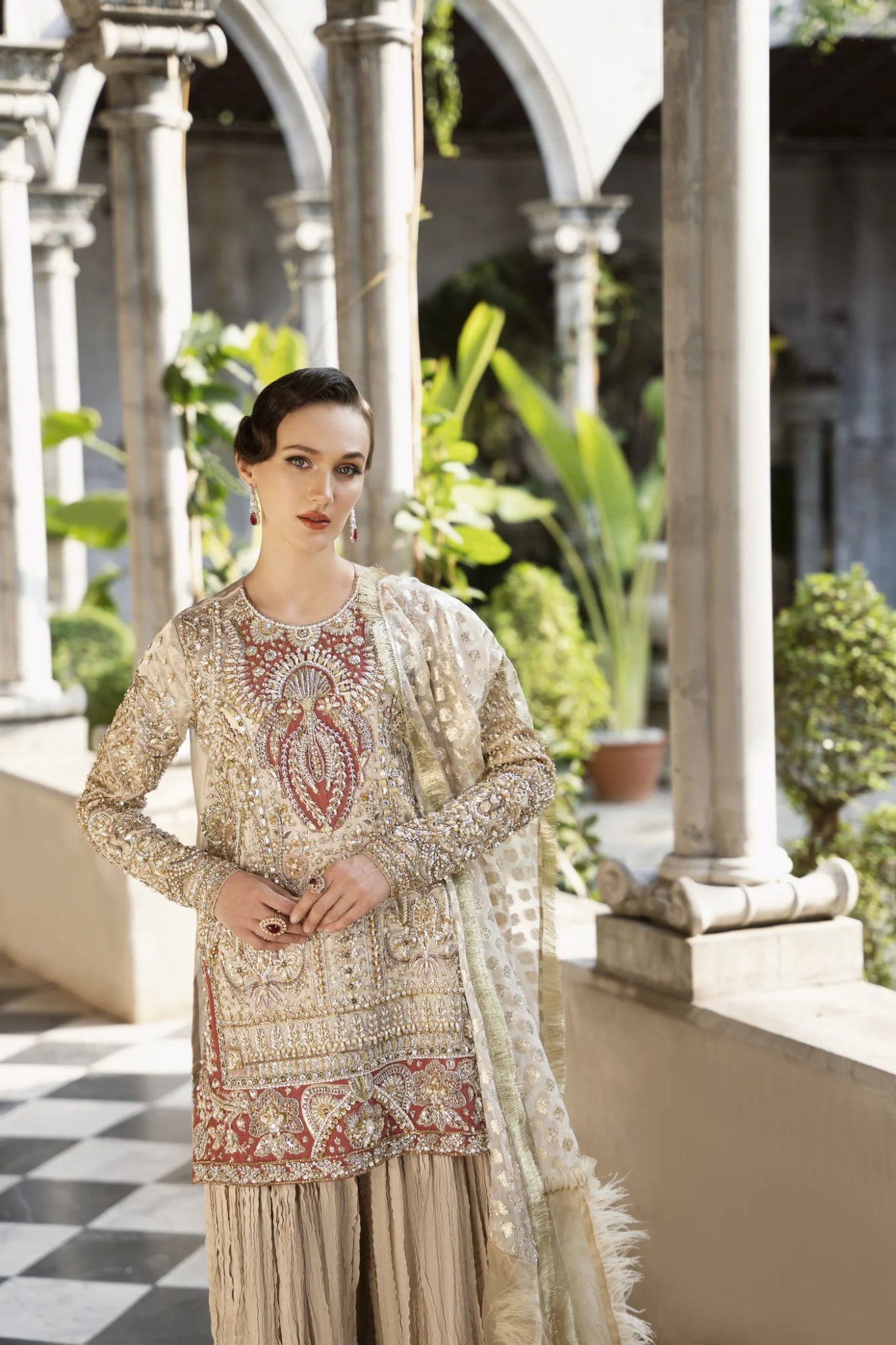 Model wearing a gold and red embellished GLEAM dress from Mysie by Tahira. Perfect for weddings, showcasing intricate embroidery. Shop Pakistani clothes online in the UK.