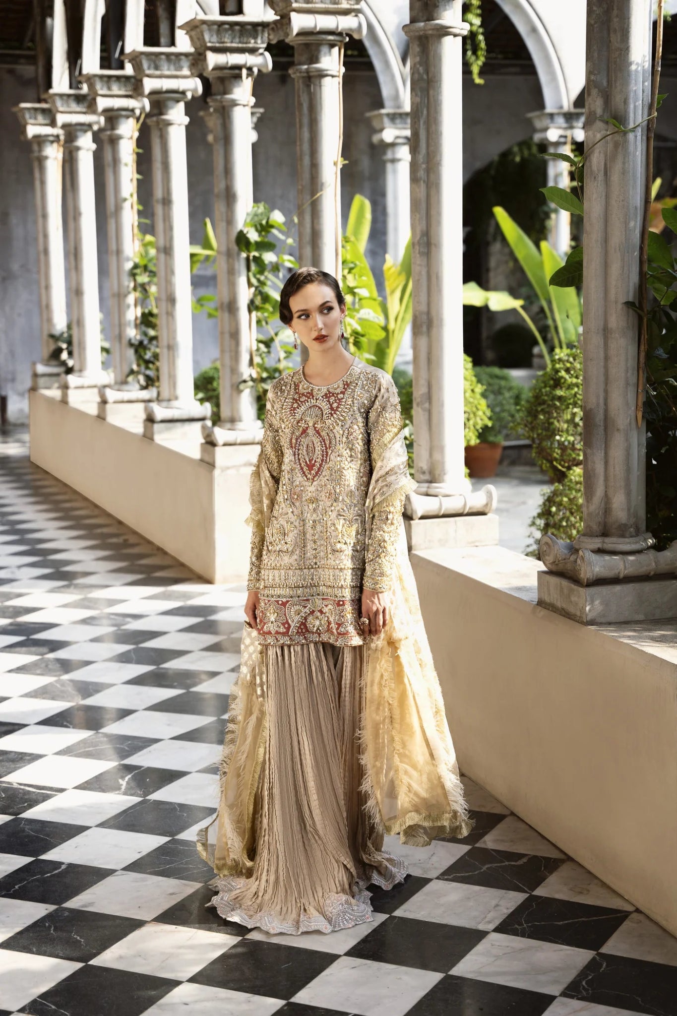 Model wearing a gold and red embellished GLEAM dress from Mysie by Tahira. Perfect for weddings, showcasing intricate embroidery. Shop Pakistani clothes online in the UK.