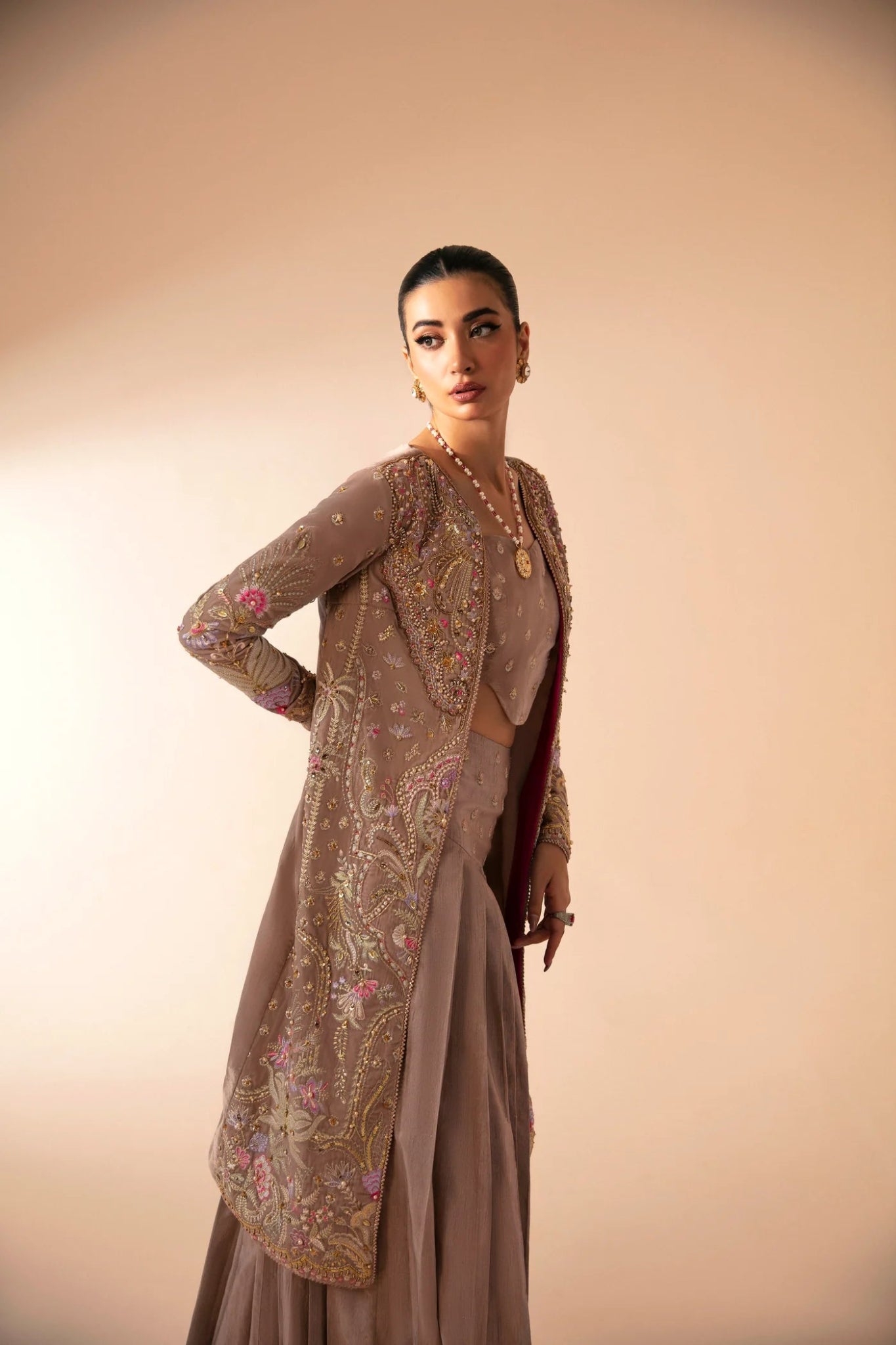 Model wearing FA'IA from Mysie by Tahira in taupe, featuring a pleated skirt and embellished jacket. Pakistani clothes online in UK, ideal for weddings and formal occasions.