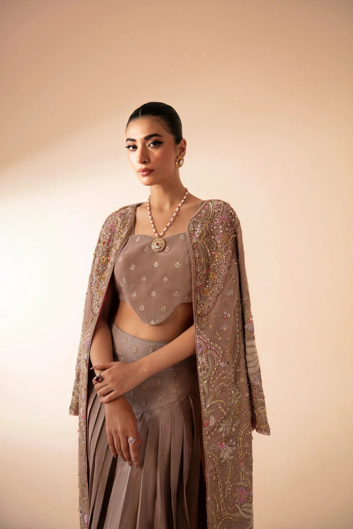 Model wearing FA'IA from Mysie by Tahira in taupe, featuring a pleated skirt and embellished jacket. Pakistani clothes online in UK, ideal for weddings and formal occasions.