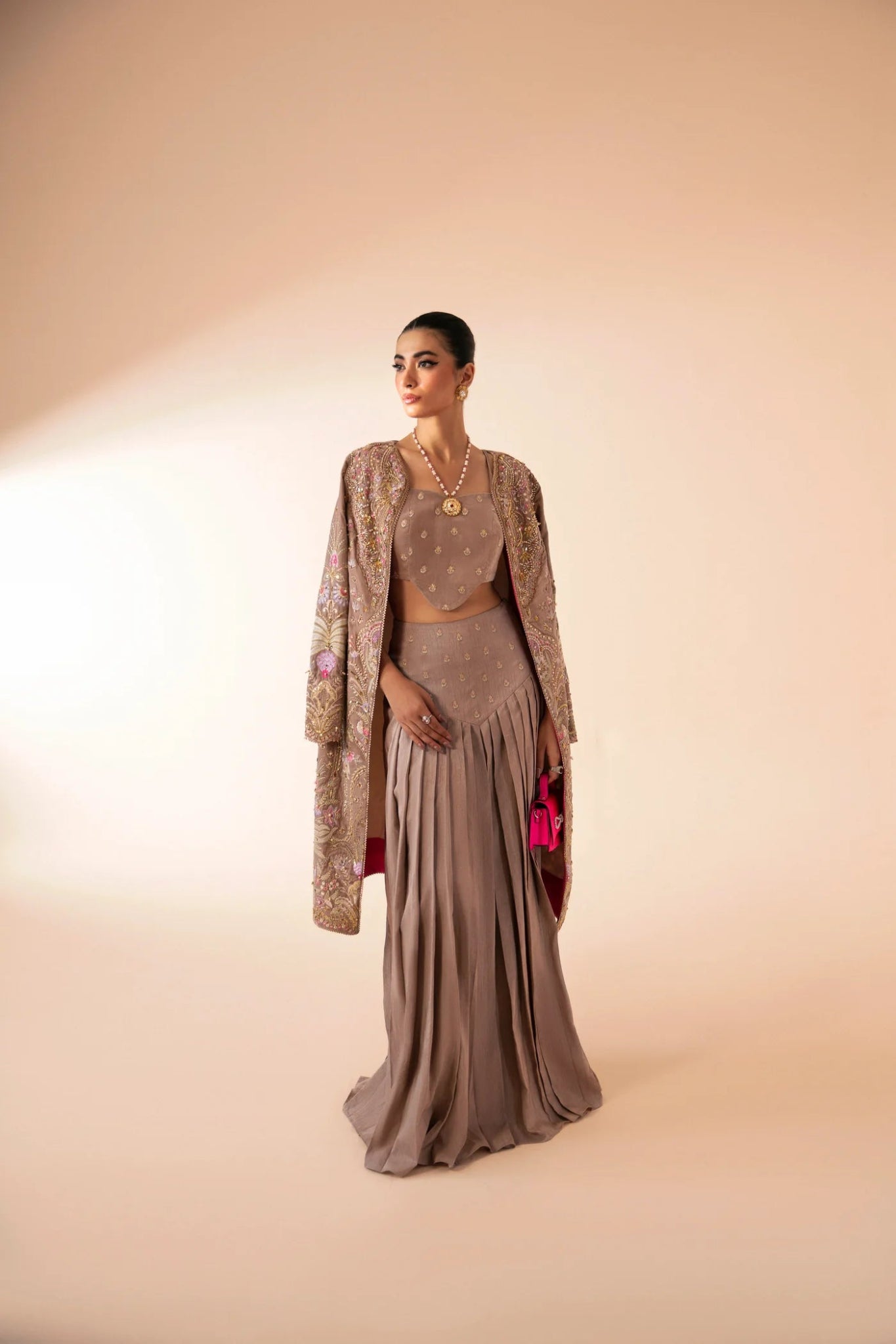 Model wearing FA'IA from Mysie by Tahira in taupe, featuring a pleated skirt and embellished jacket. Pakistani clothes online in UK, ideal for weddings and formal occasions.