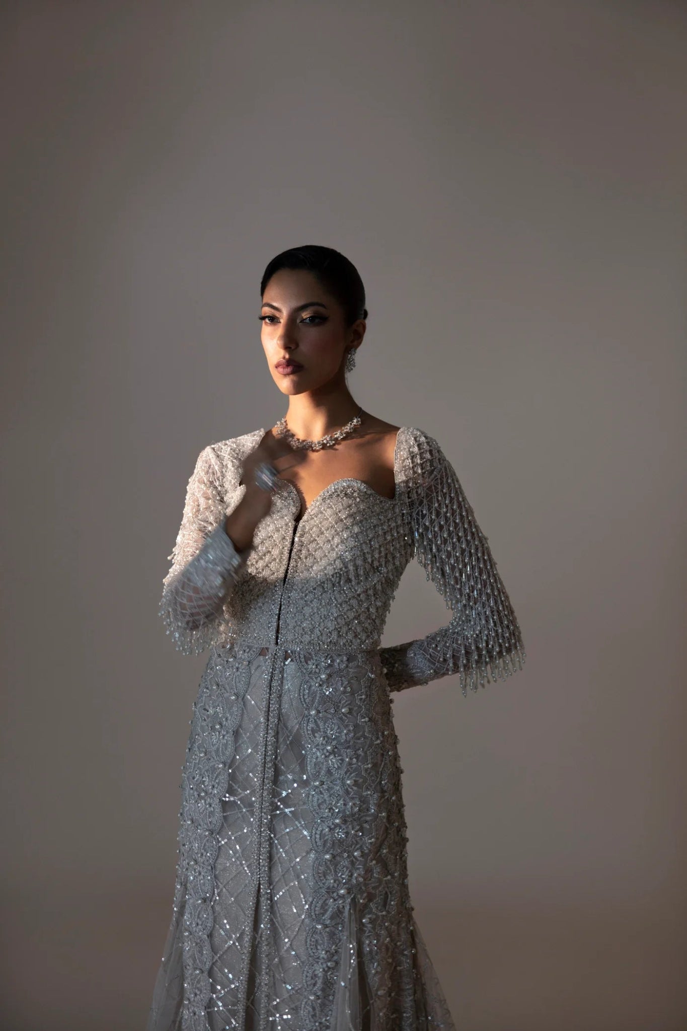 Model wearing Ferē from Mysie by Tahira in a silver embellished gown with long sleeves. Pakistani wedding clothes online in UK, perfect for formal events.