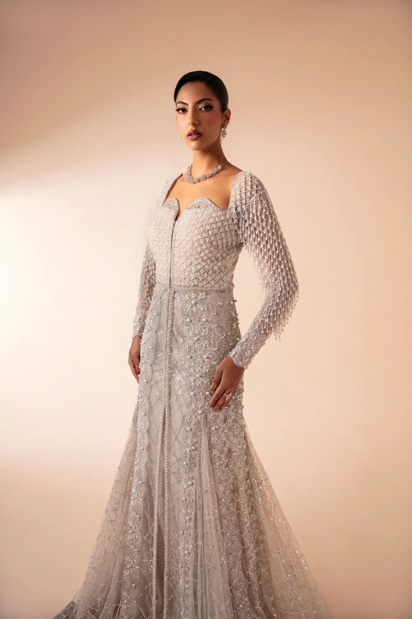 Model wearing Ferē from Mysie by Tahira in a silver embellished gown with long sleeves. Pakistani wedding clothes online in UK, perfect for formal events.