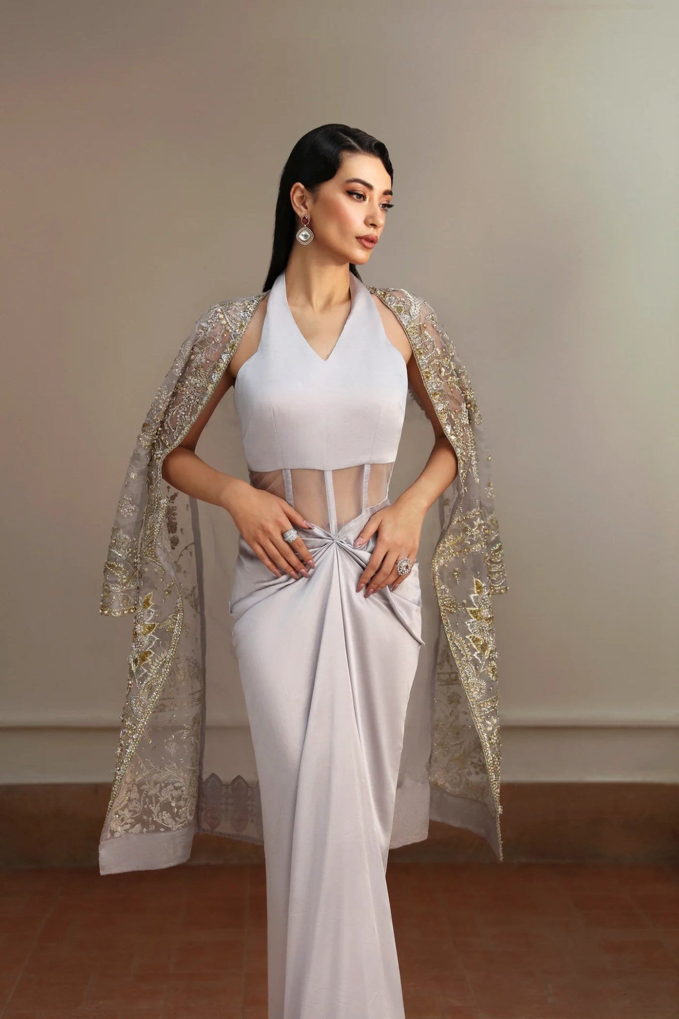 Model wearing Fiza from Mysie by Tahira in a silver embellished formal gown with sheer long sleeves and a fitted silhouette. Pakistani wedding clothes online in UK.