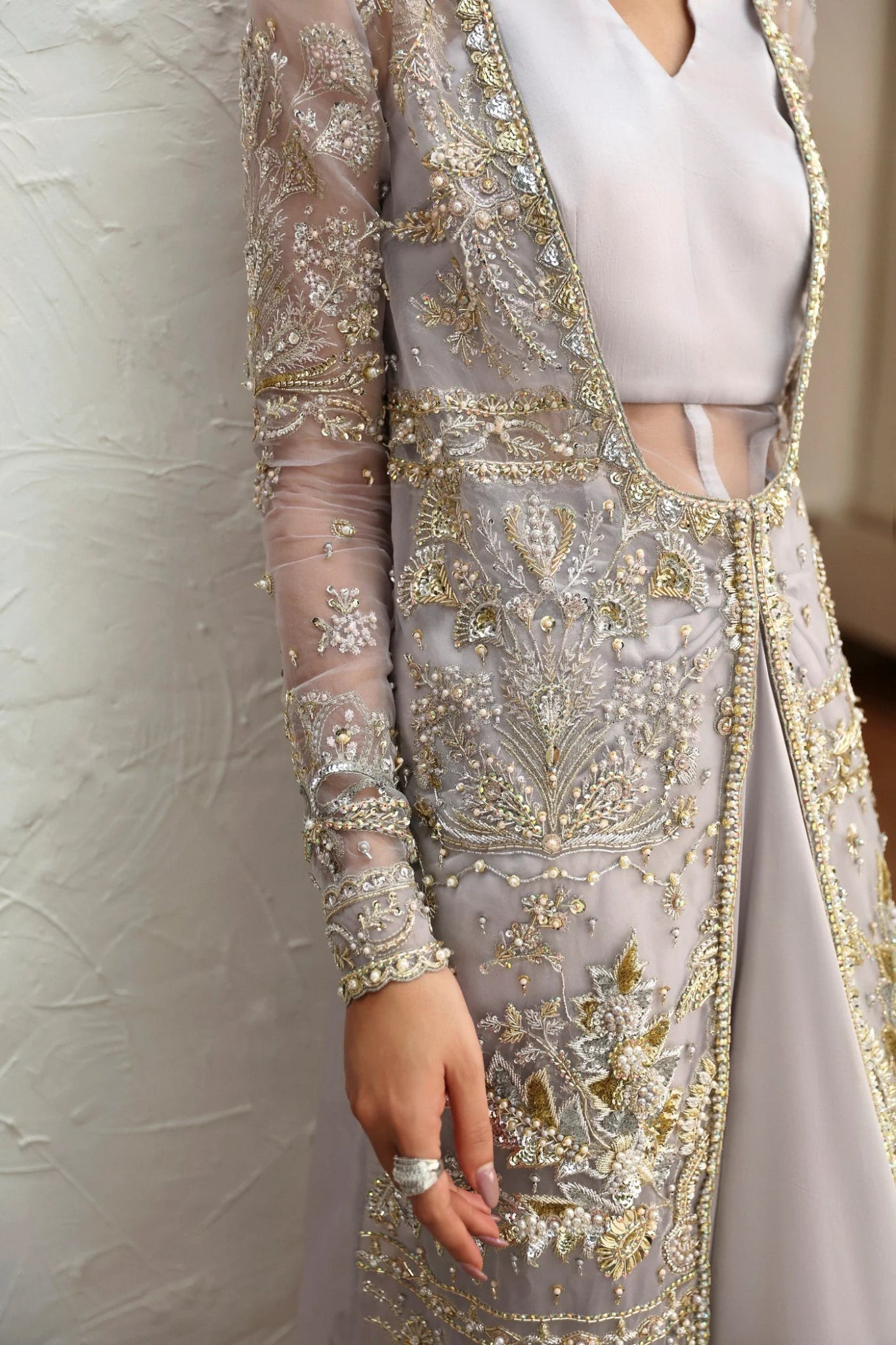 Model wearing Fiza from Mysie by Tahira in a silver embellished formal gown with sheer long sleeves and a fitted silhouette. Pakistani wedding clothes online in UK.