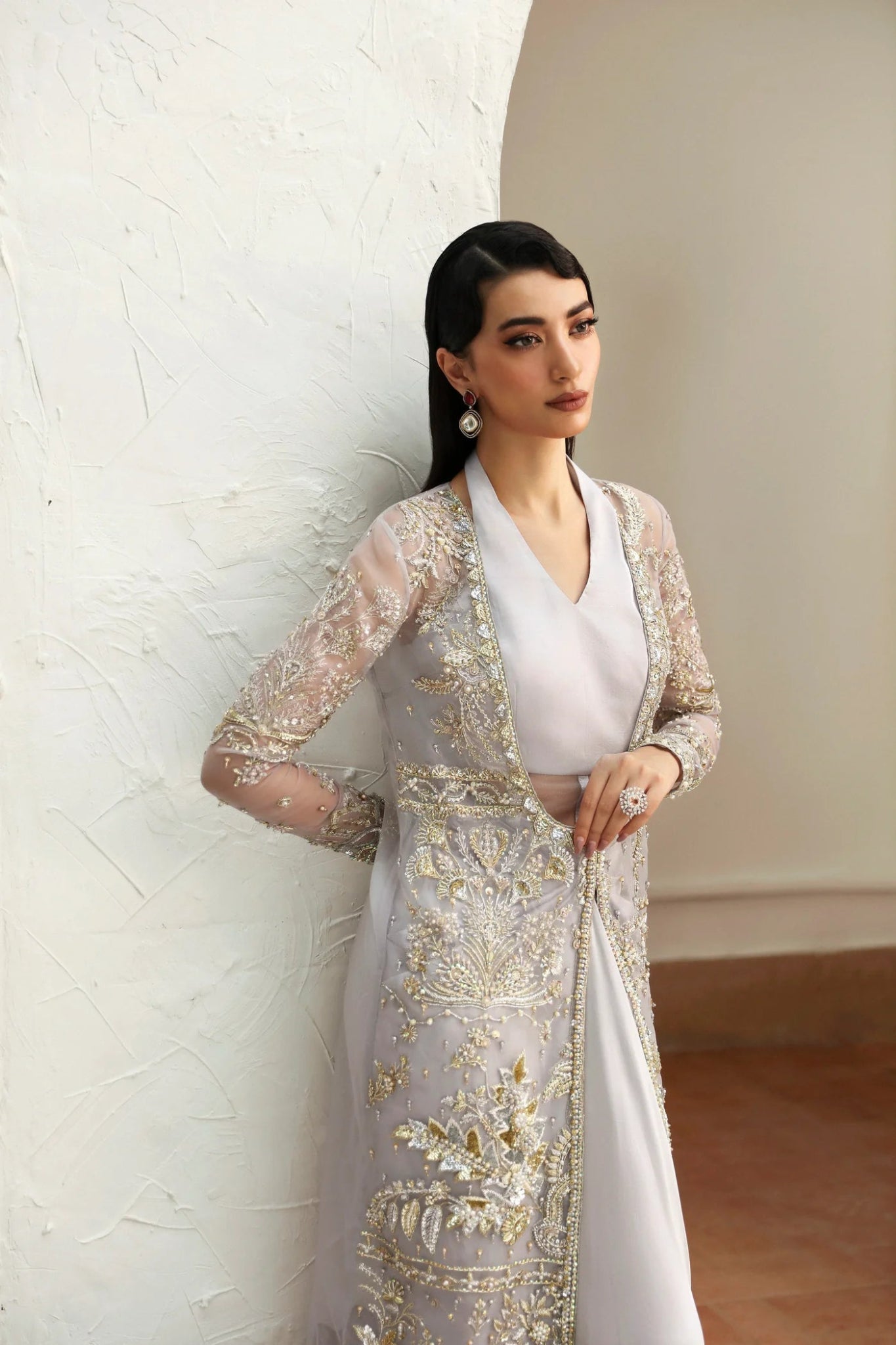 Model wearing Fiza from Mysie by Tahira in a silver embellished formal gown with sheer long sleeves and a fitted silhouette. Pakistani wedding clothes online in UK.