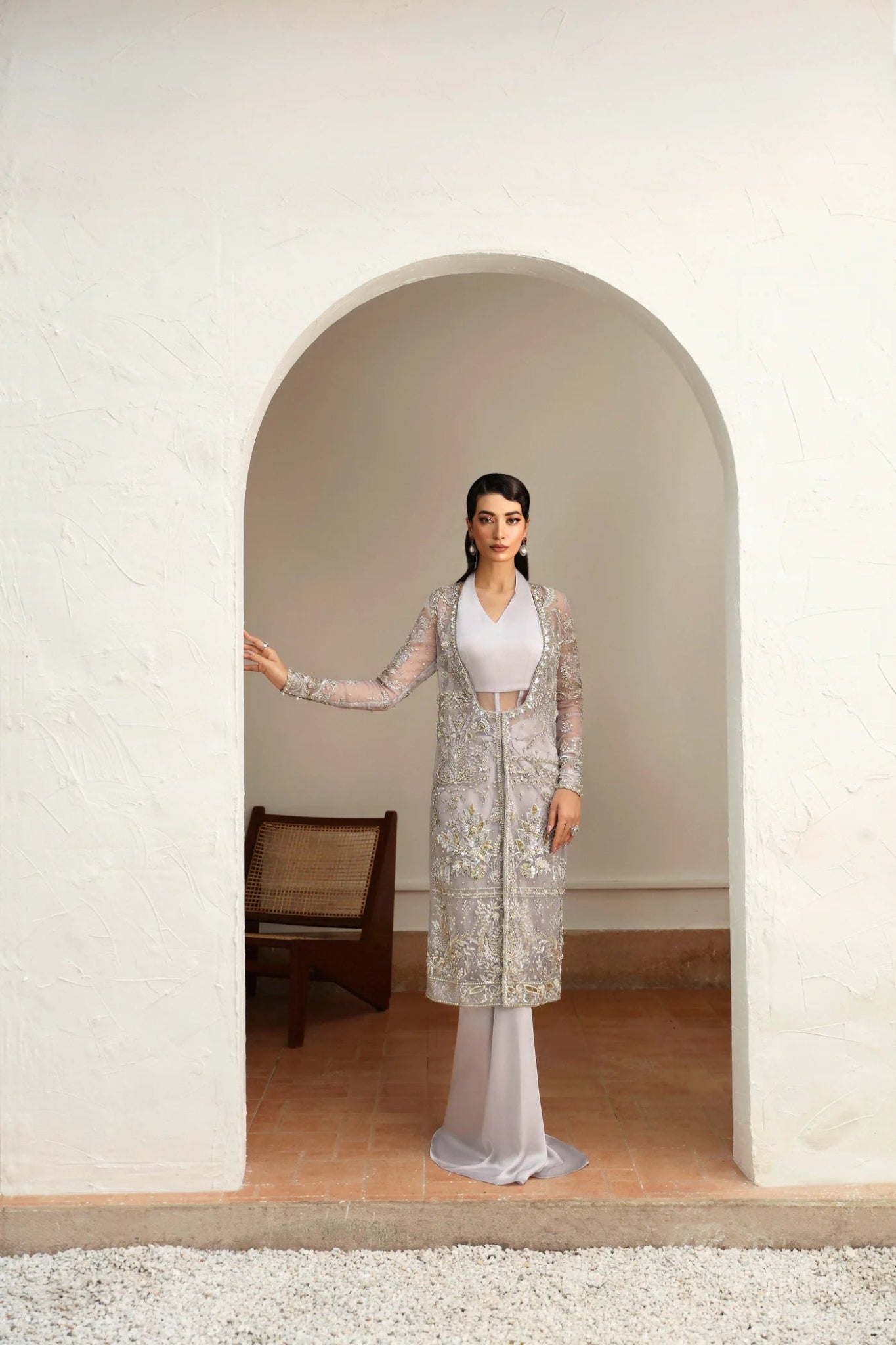 Model wearing Fiza from Mysie by Tahira in a silver embellished formal gown with sheer long sleeves and a fitted silhouette. Pakistani wedding clothes online in UK.