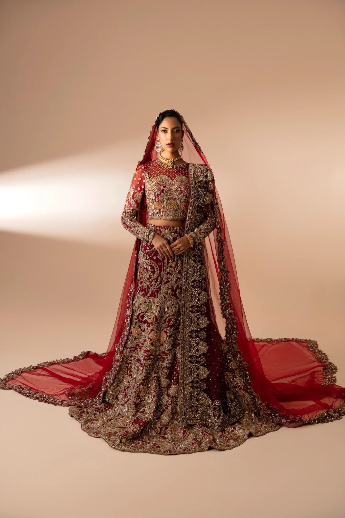 Model wearing Leela from Mysie by Tahira in a red and gold heavily embellished bridal lehenga. Pakistani wedding clothes online in UK.