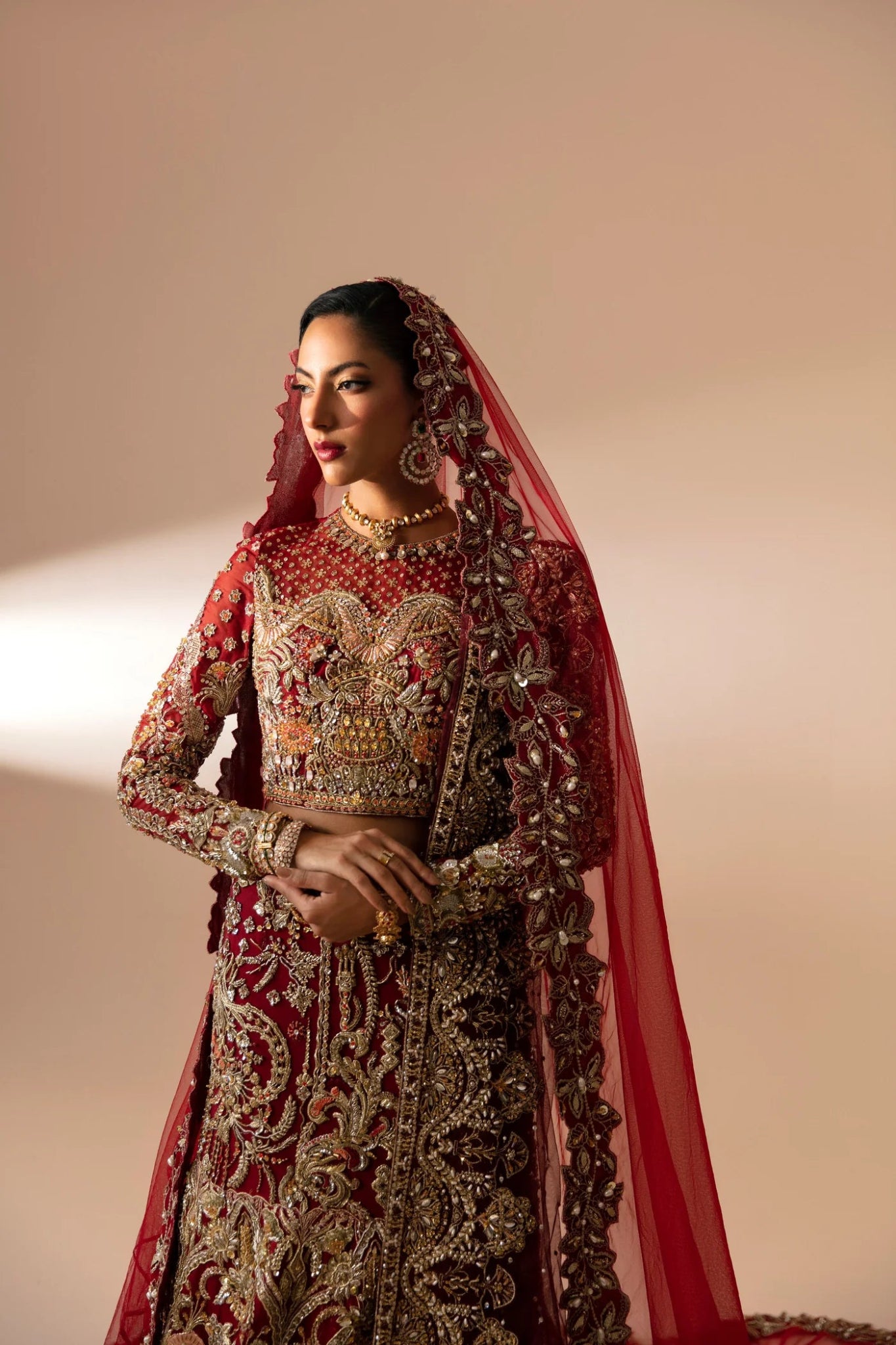 Model wearing Leela from Mysie by Tahira in a red and gold heavily embellished bridal lehenga. Pakistani wedding clothes online in UK.