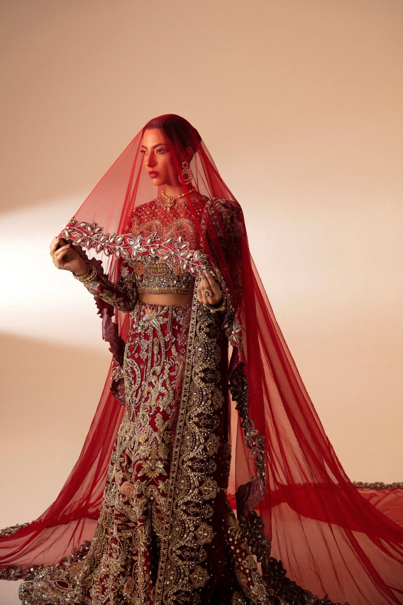 Model wearing Leela from Mysie by Tahira in a red and gold heavily embellished bridal lehenga. Pakistani wedding clothes online in UK.