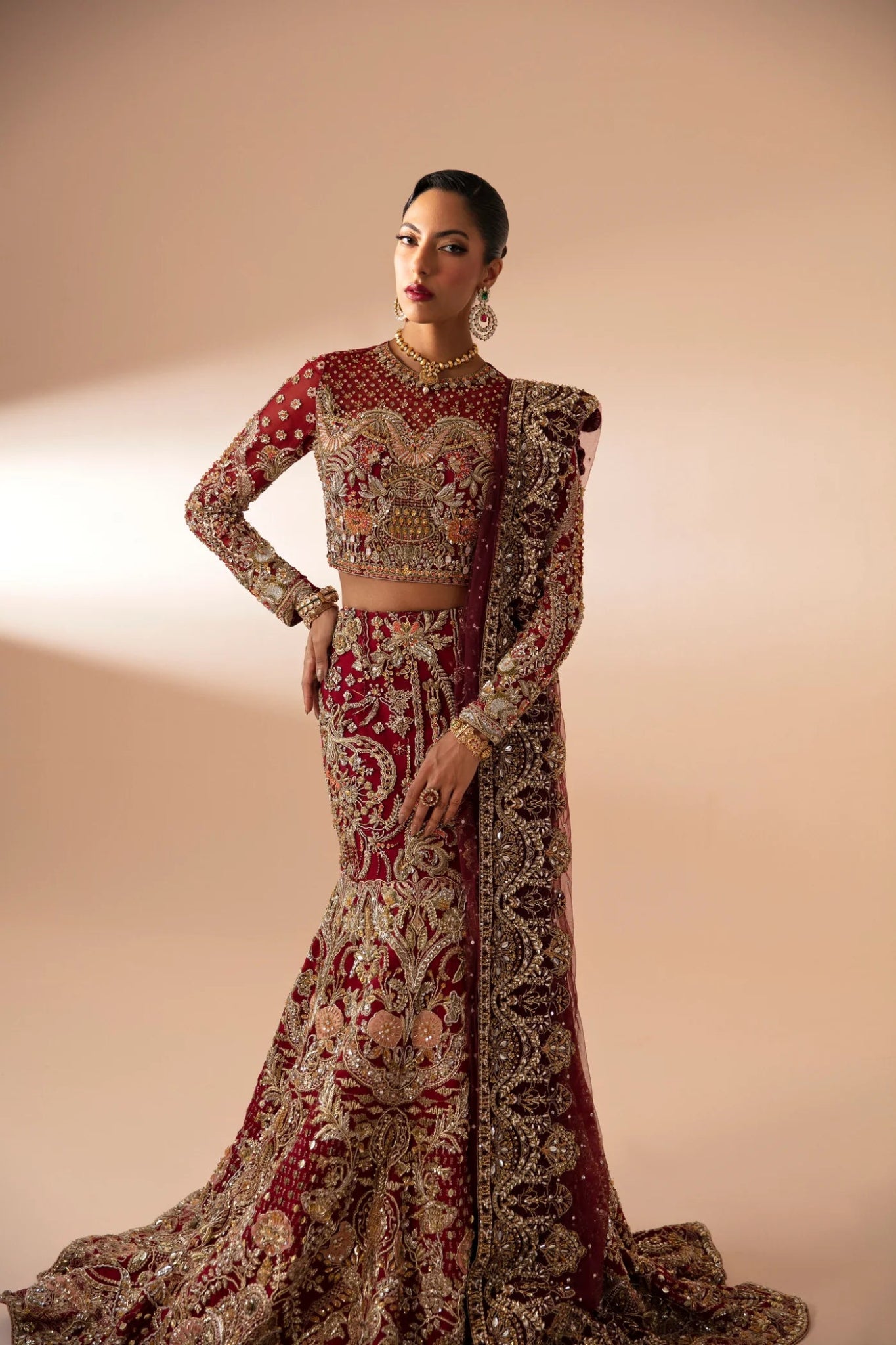 Model wearing Leela from Mysie by Tahira in a red and gold heavily embellished bridal lehenga. Pakistani wedding clothes online in UK.