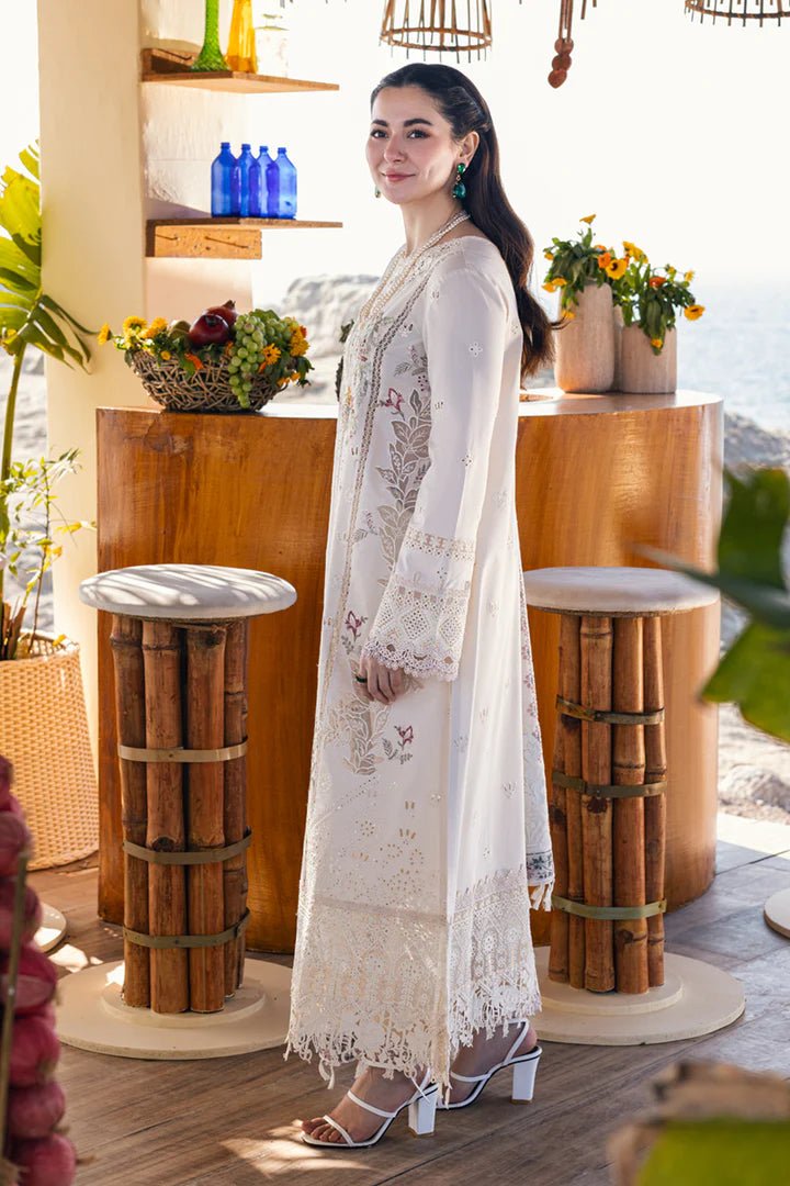 Model wearing a white FP - 12 MARWA dress from Qalamkar with intricate embroidery, standing against a beach background. Pakistani clothes online in UK, lawn suits.