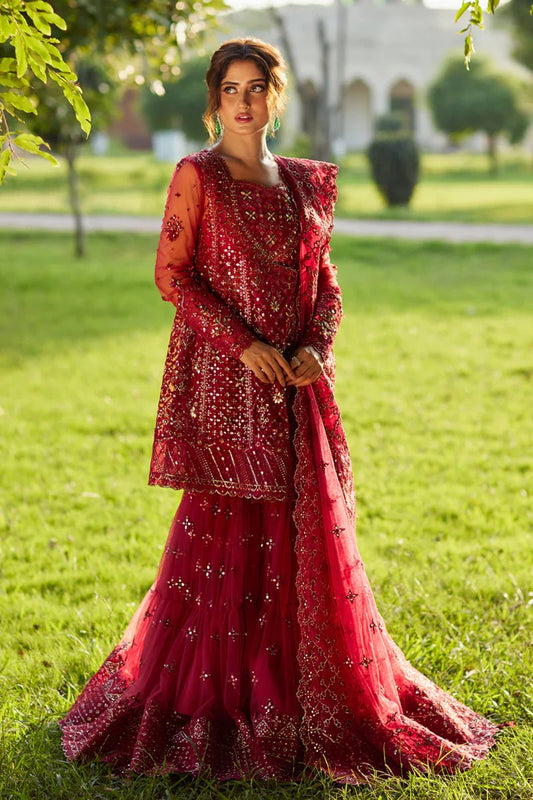 Model wearing Qalamkaar Shadmani Luxury Formals '24 Nurah SH - 07 dress in deep red with intricate gold embellishments. Shop Pakistani bridal dresses online in the UK now.