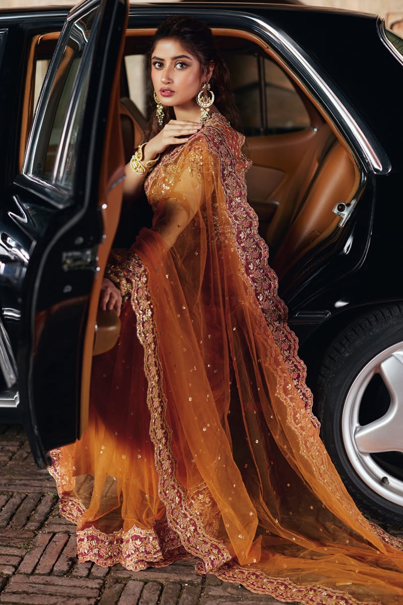 Model wearing Qalamkaar Shadmani Luxury Formals '24 Raniya SH - 02 dress in burnt orange with intricate gold embroidery. Shop Pakistani bridal dresses online in the UK now.