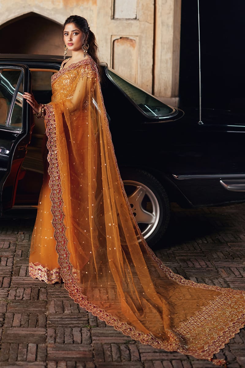 Model wearing Qalamkaar Shadmani Luxury Formals '24 Raniya SH - 02 dress in burnt orange with intricate gold embroidery. Shop Pakistani bridal dresses online in the UK now.