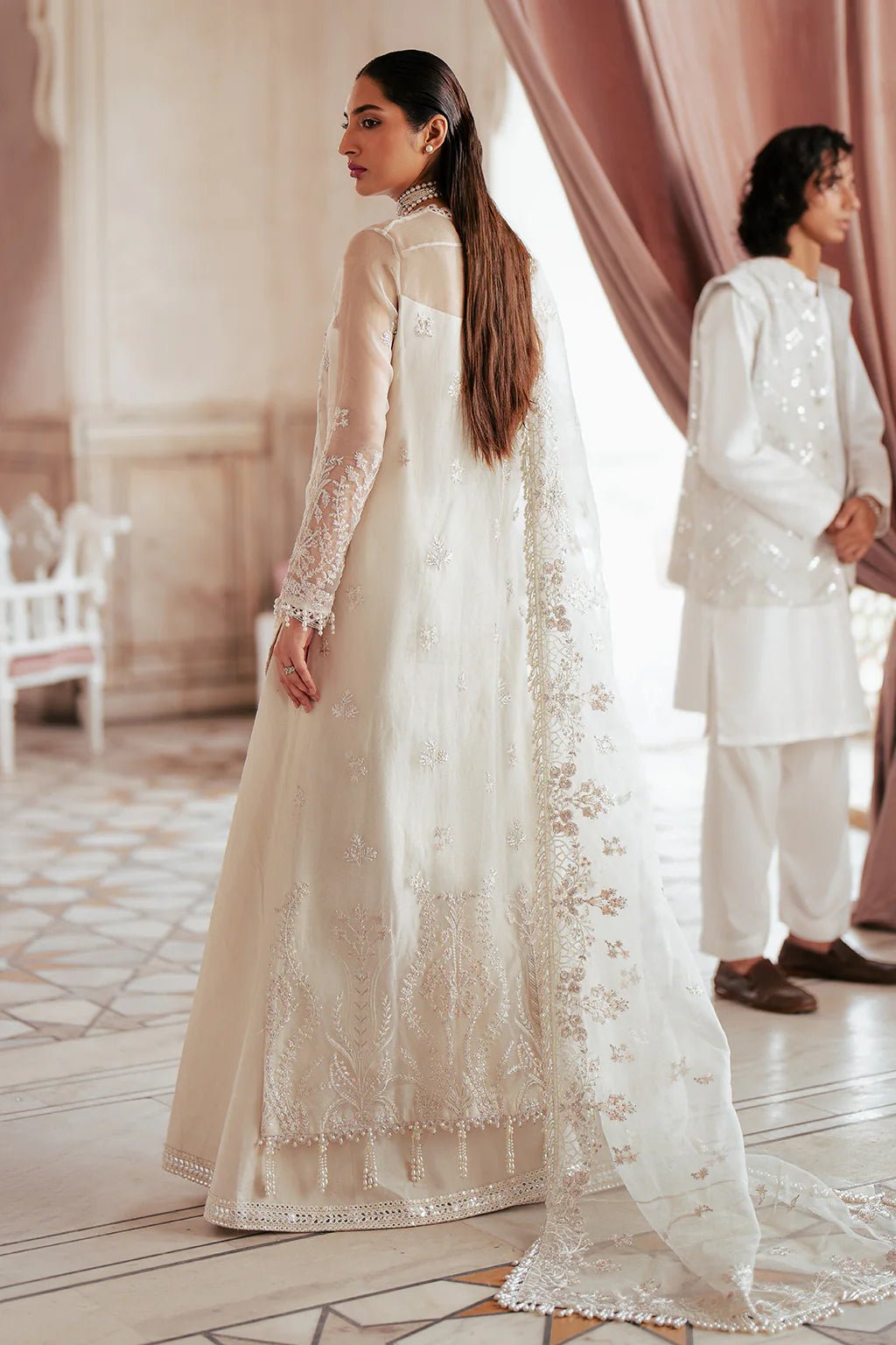 A model wearing an elegant off - white Saad Shiekh ensemble from collection Silsila with intricate organza embroidery, an embroidered dupatta with detailed pallu, and complementing raw silk trousers.