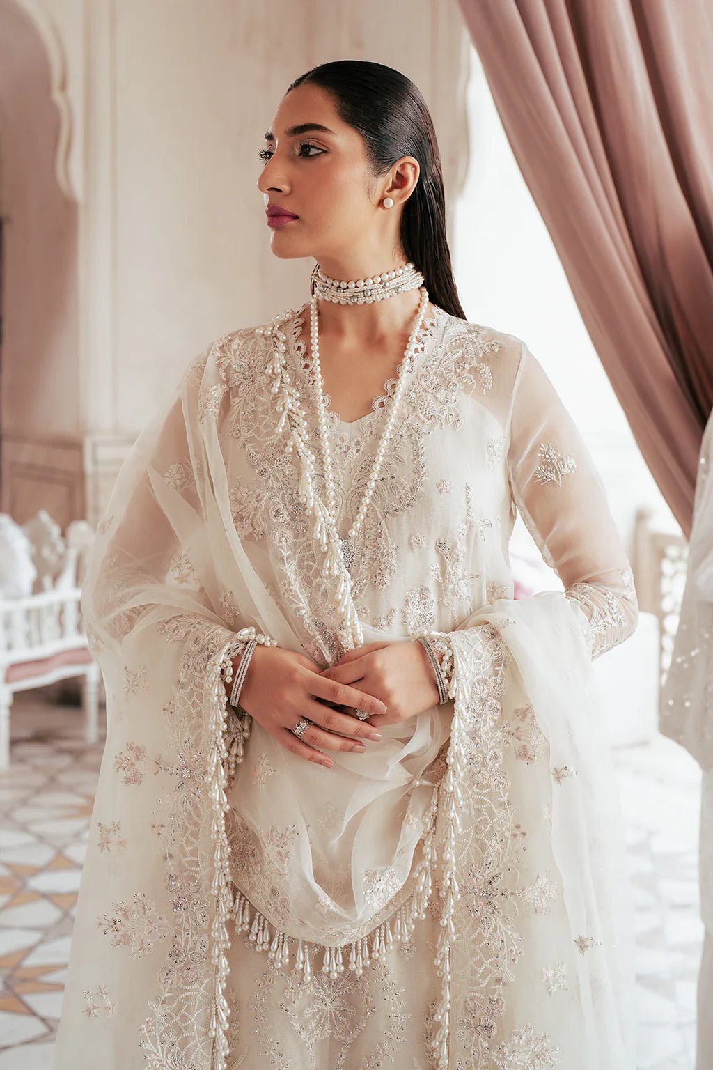 A model wearing an elegant off - white Saad Shiekh ensemble from collection Silsila with intricate organza embroidery, an embroidered dupatta with detailed pallu, and complementing raw silk trousers.