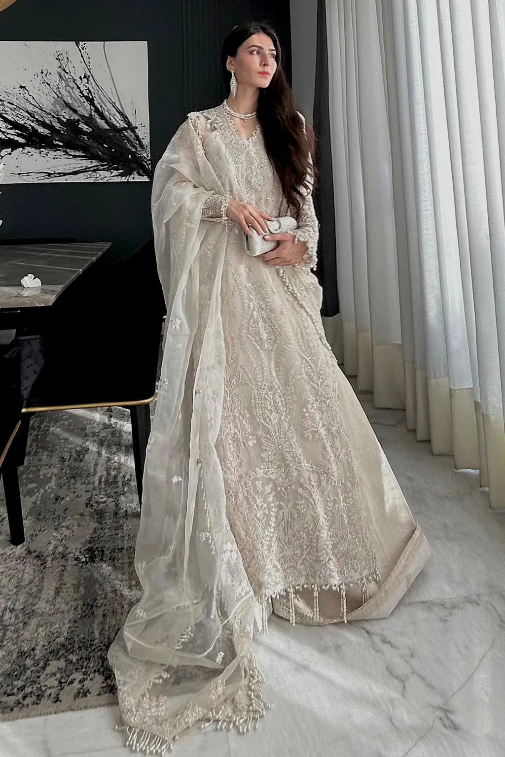 A model wearing an elegant off - white Saad Shiekh ensemble from collection Silsila with intricate organza embroidery, an embroidered dupatta with detailed pallu, and complementing raw silk trousers.