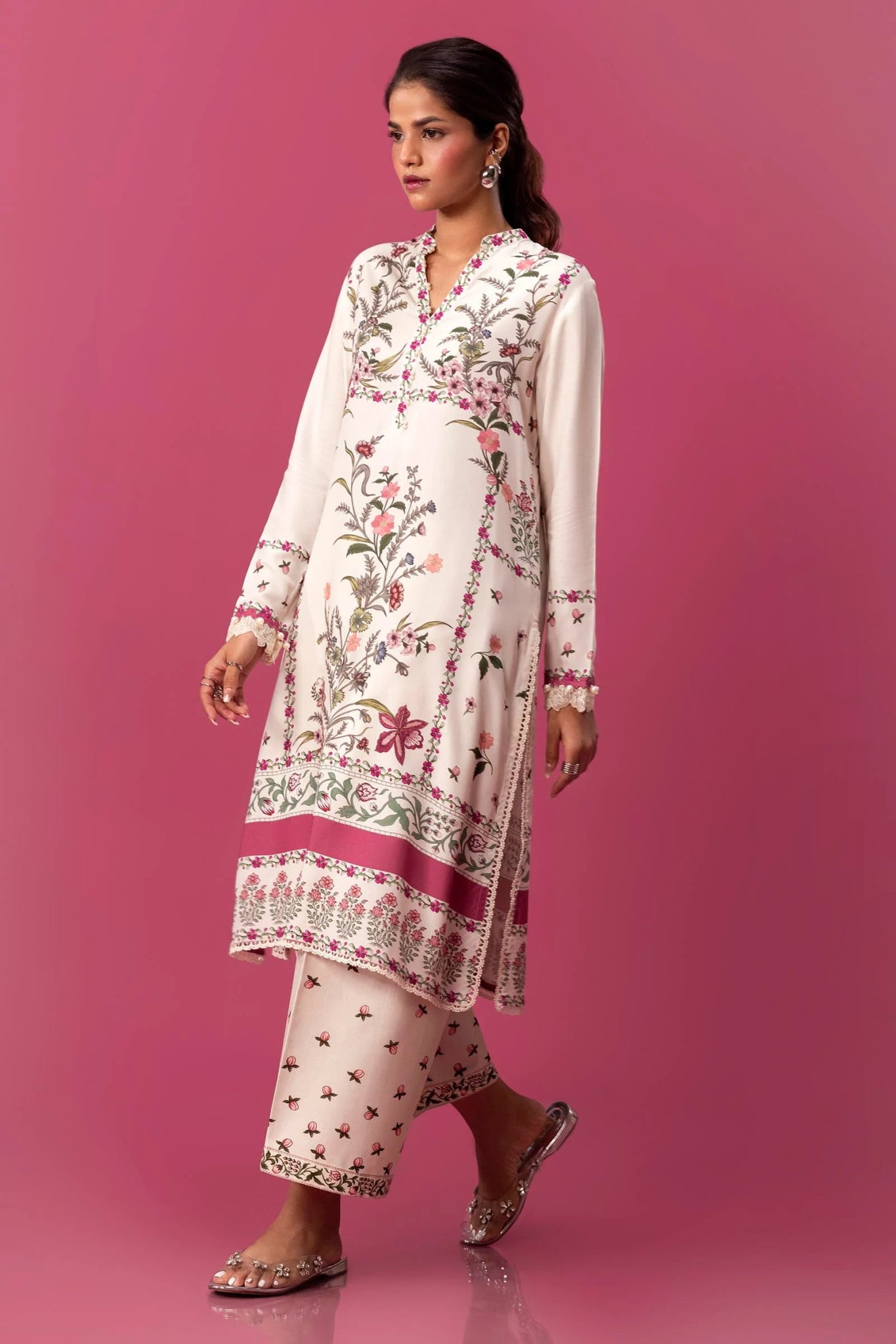 Model wearing a two - piece Sana Safinaz suit from Mahay Winter '24 with floral digital prints on a white linen shirt, embroidered organza patti, and matching cambric pants. Available online in the UK.