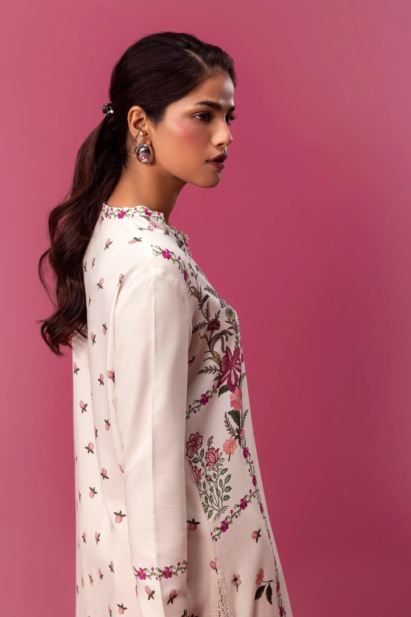 Model wearing a two - piece Sana Safinaz suit from Mahay Winter '24 with floral digital prints on a white linen shirt, embroidered organza patti, and matching cambric pants. Available online in the UK.