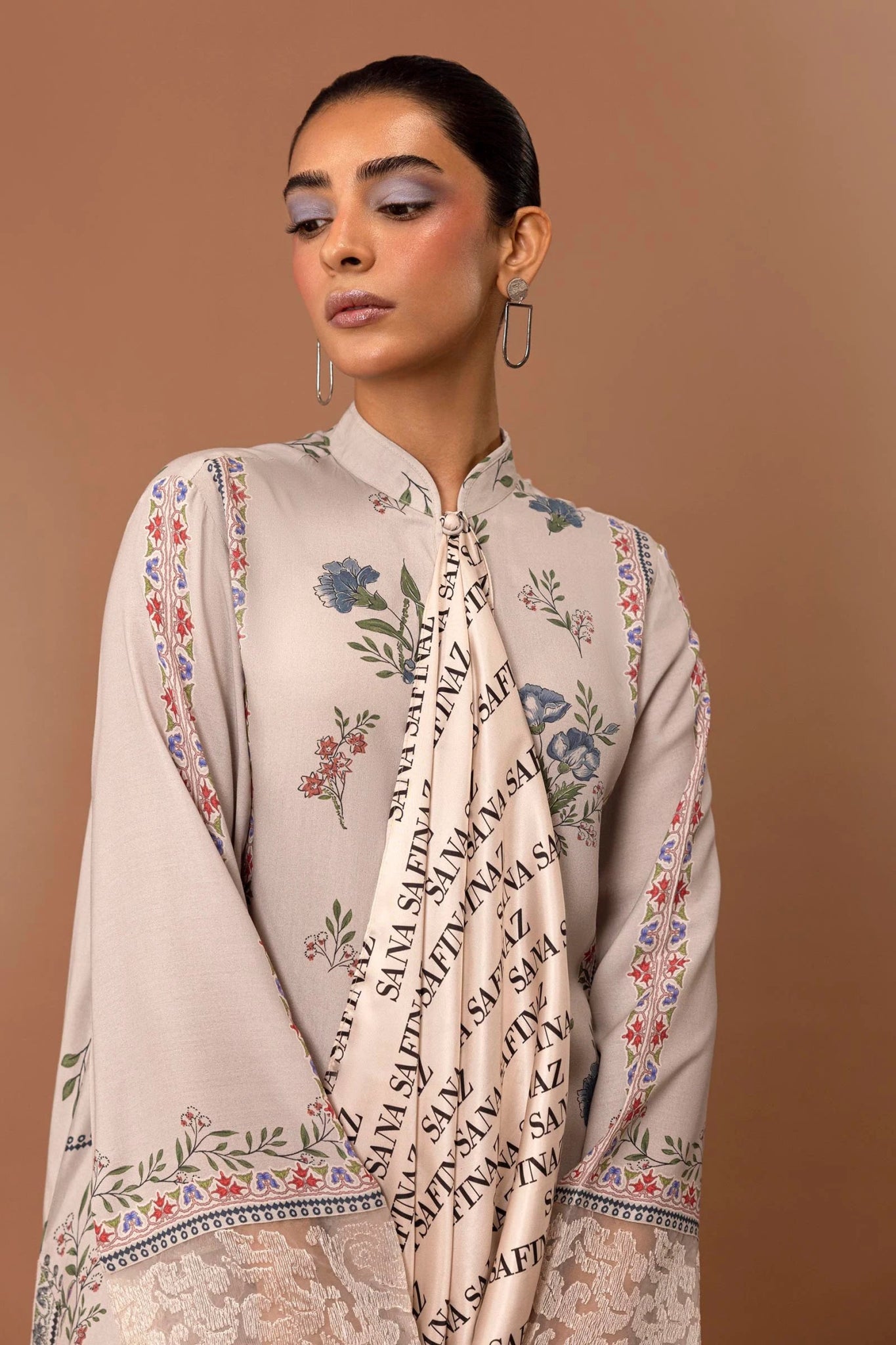 Model wearing a two - piece Sana Safinaz suit from Mahay Winter '24 in beige, featuring floral digital prints, embroidered organza patti, and printed cambric pants. Available online in the UK.