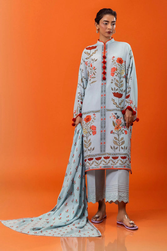 Model wearing a three - piece Sana Safinaz suit from Mahay Winter '24 in light blue, featuring floral digital prints on linen, a matching printed dupatta, and dyed cambric pants with lace detailing. Available online in the UK.