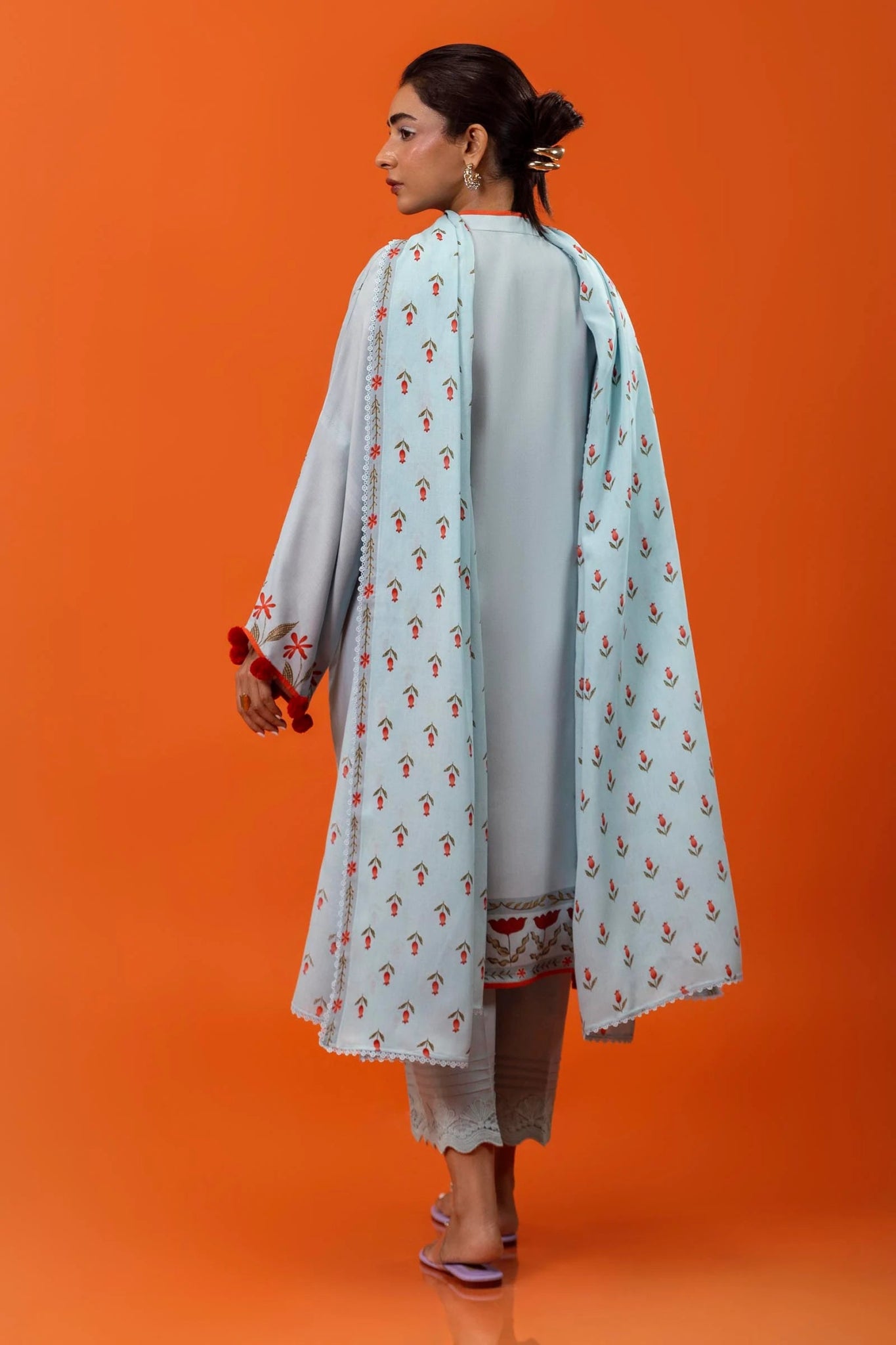 Model wearing a three - piece Sana Safinaz suit from Mahay Winter '24 in light blue, featuring floral digital prints on linen, a matching printed dupatta, and dyed cambric pants with lace detailing. Available online in the UK.