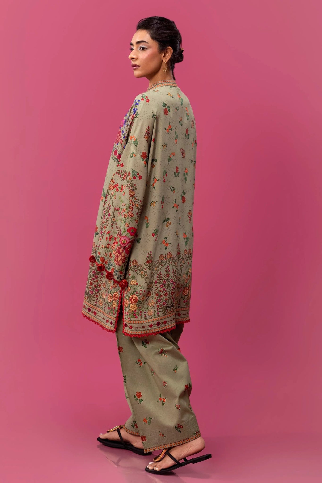 Model wearing a two - piece Sana Safinaz suit from Mahay Winter '24 in olive green, featuring vibrant floral digital prints on a linen shirt, and matching cambric pants. Available online in the UK.