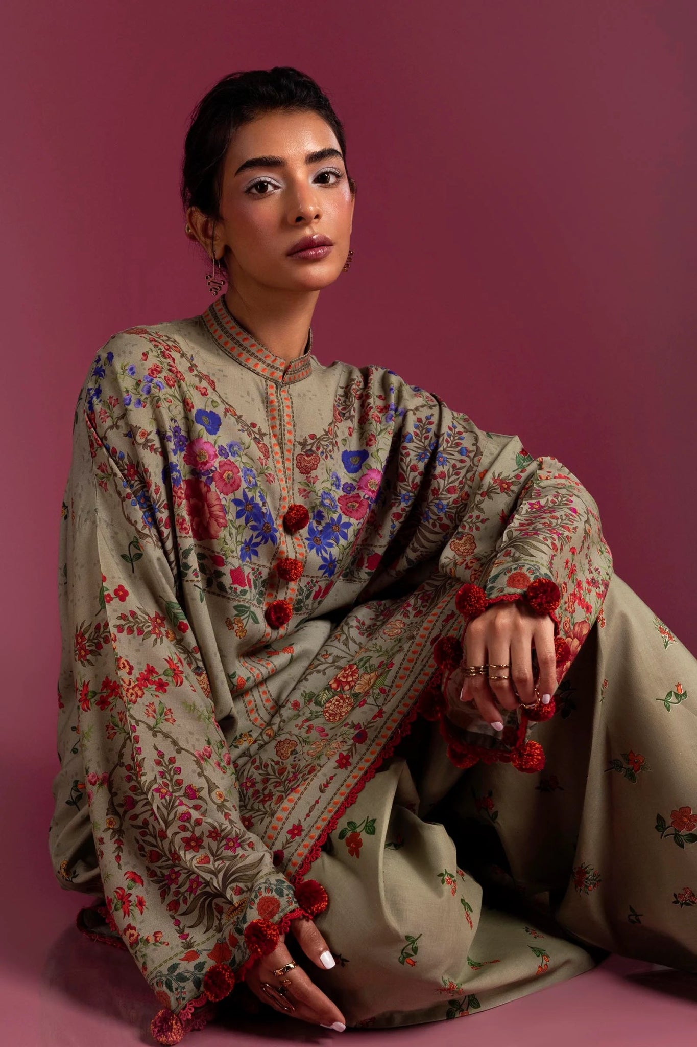 Model wearing a two - piece Sana Safinaz suit from Mahay Winter '24 in olive green, featuring vibrant floral digital prints on a linen shirt, and matching cambric pants. Available online in the UK.