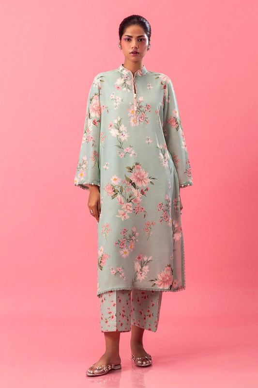 Model wearing a two - piece Sana Safinaz suit from Mahay Winter '24 in mint green, featuring soft floral digital prints on a linen shirt with embroidered organza details and matching cambric pants. Available online in the UK.