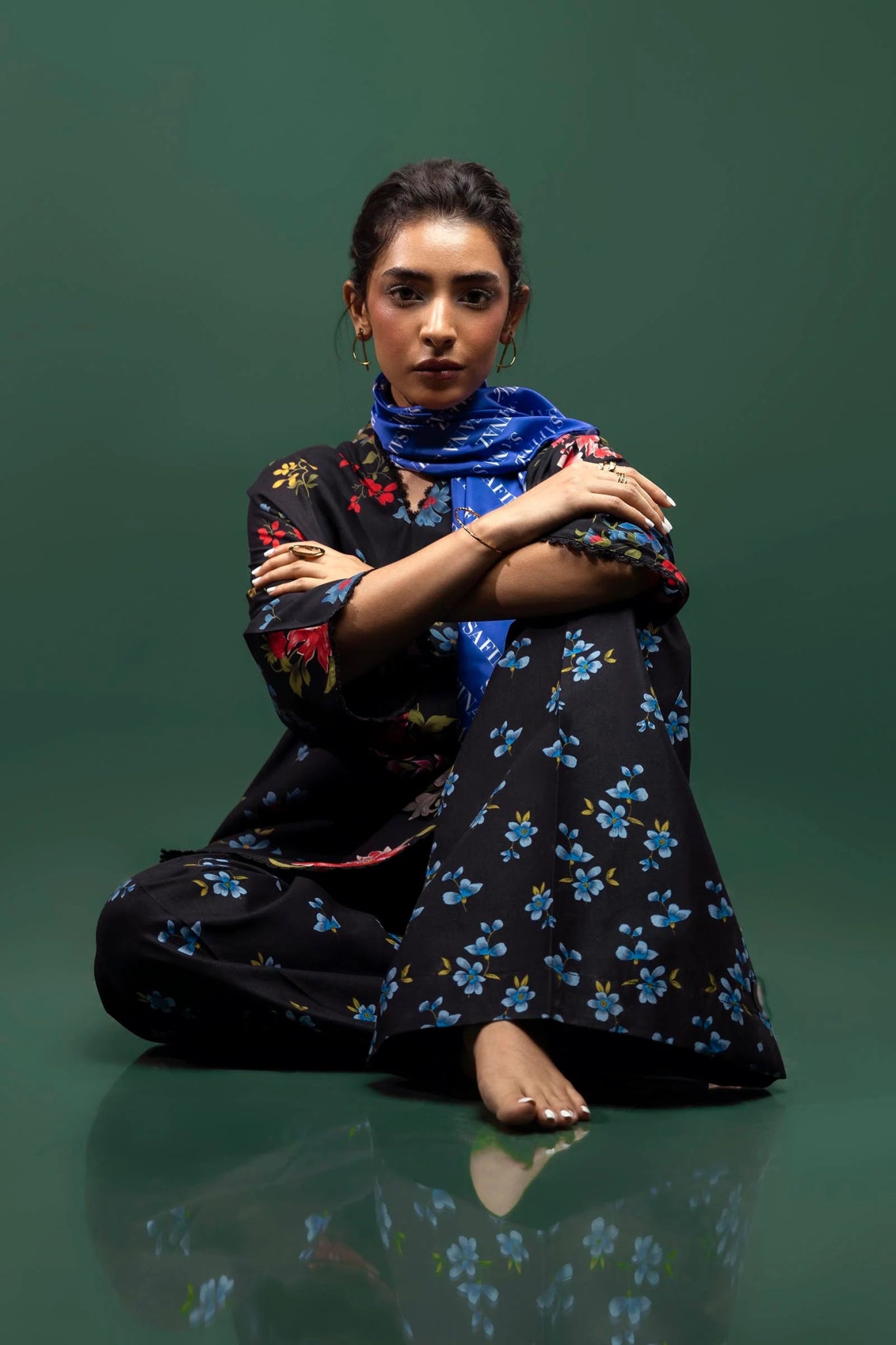 Model wearing a two - piece Sana Safinaz suit from Mahay Winter '24 featuring a black linen shirt with vibrant floral prints, embroidered organza accents, and matching printed cambric pants. Available online in the UK.