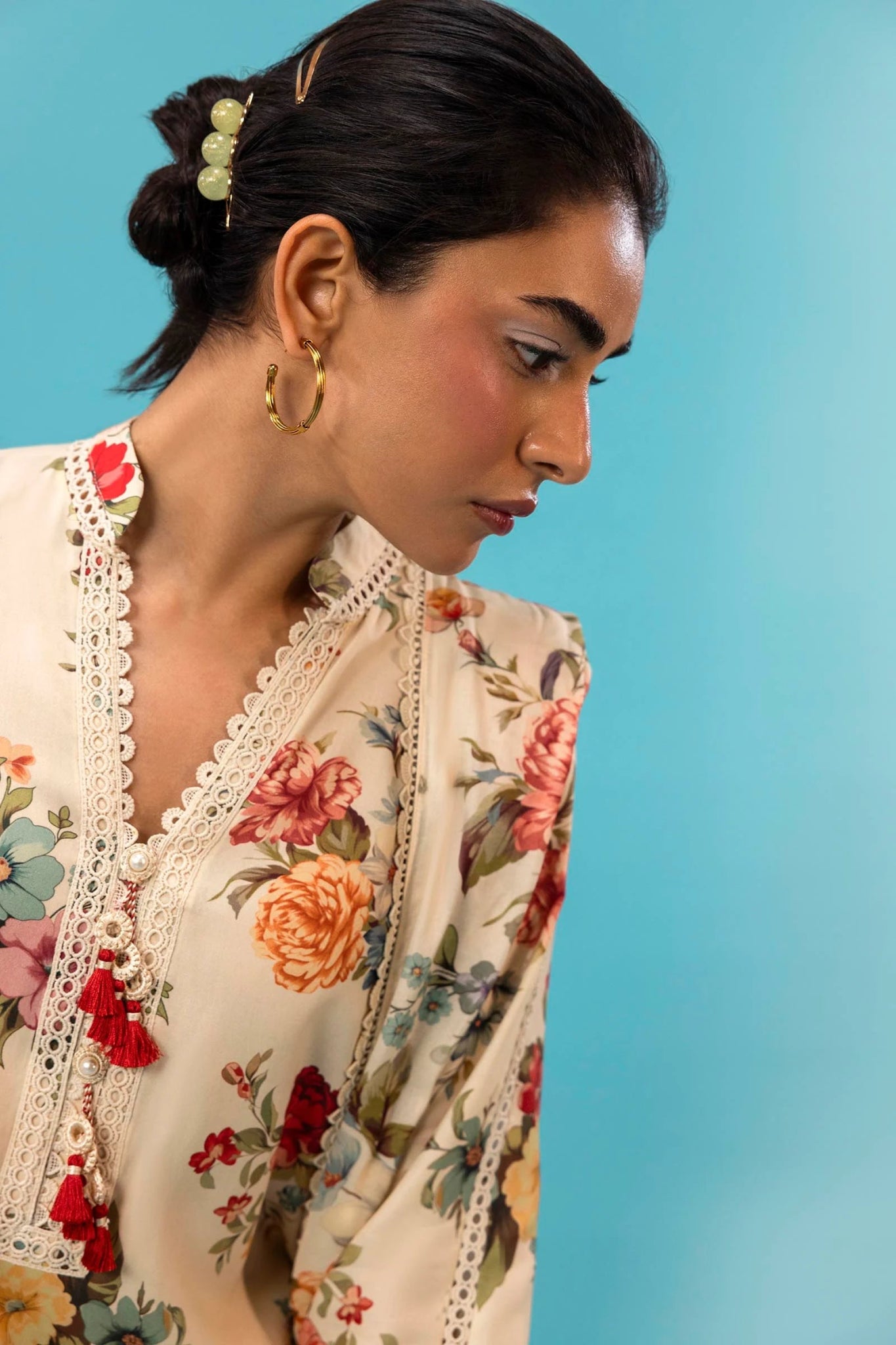 Model wearing a three - piece Sana Safinaz suit from Mahay Winter '24 featuring a cream linen shirt with vibrant floral prints, a matching printed dupatta, and striped cambric pants. Available online in the UK.