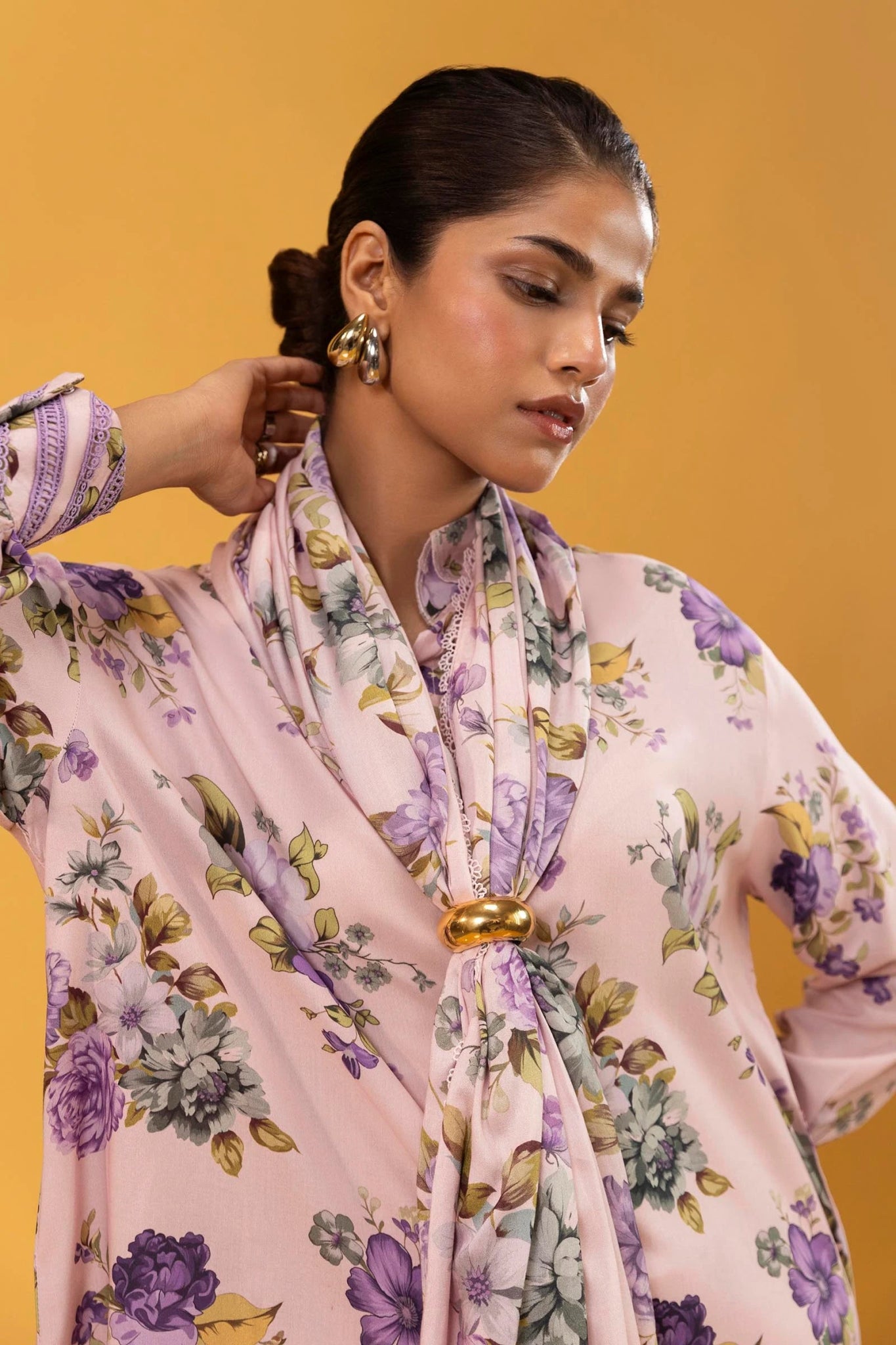 Model wearing a three - piece Sana Safinaz suit from Mahay Winter '24 in pastel pink, featuring delicate floral digital prints on a linen shirt, matching printed dupatta, and striped cambric pants. Available online in the UK.