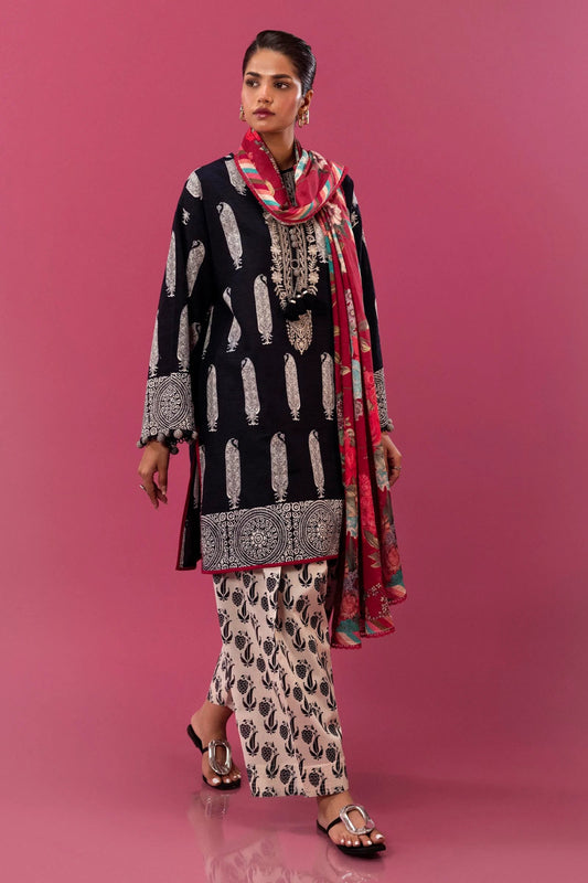 Model wearing a three - piece Sana Safinaz suit from Mahay Winter '24 in black, featuring intricate rotary prints on slub fabric, an embroidered organza neckline, a vibrant digital printed khaddar dupatta, and matching cambric pants. Available online in the UK.