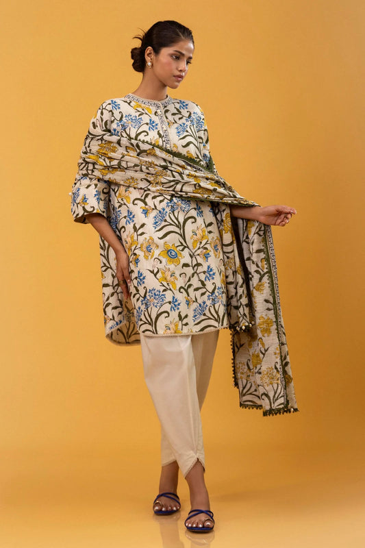 Model wearing a two - piece Sana Safinaz suit from Mahay Winter '24, featuring a cream slub shirt with blue and yellow floral rotary prints, and a matching khaddar dupatta. Available online in the UK.