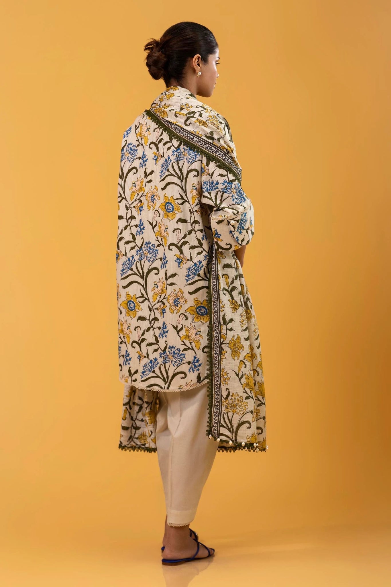 Model wearing a two - piece Sana Safinaz suit from Mahay Winter '24, featuring a cream slub shirt with blue and yellow floral rotary prints, and a matching khaddar dupatta. Available online in the UK.