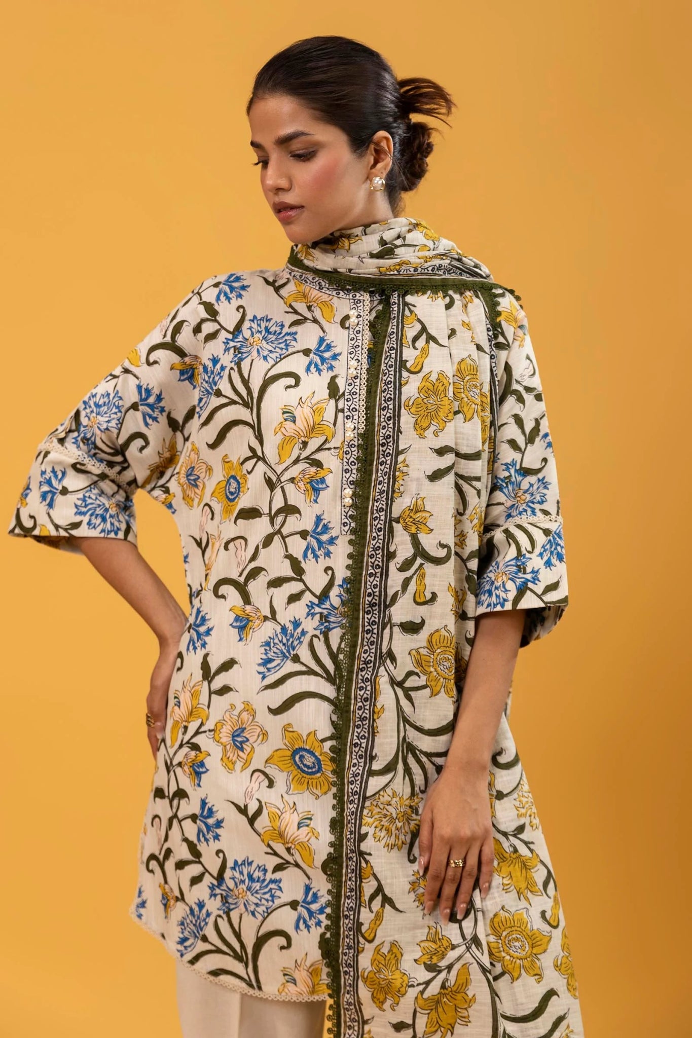 Model wearing a two - piece Sana Safinaz suit from Mahay Winter '24, featuring a cream slub shirt with blue and yellow floral rotary prints, and a matching khaddar dupatta. Available online in the UK.