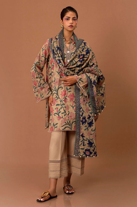 Model wearing a two - piece Sana Safinaz suit from Mahay Winter '24, featuring a beige slub shirt with intricate floral prints, delicate lace trim, and a matching printed dupatta. Available online in the UK.