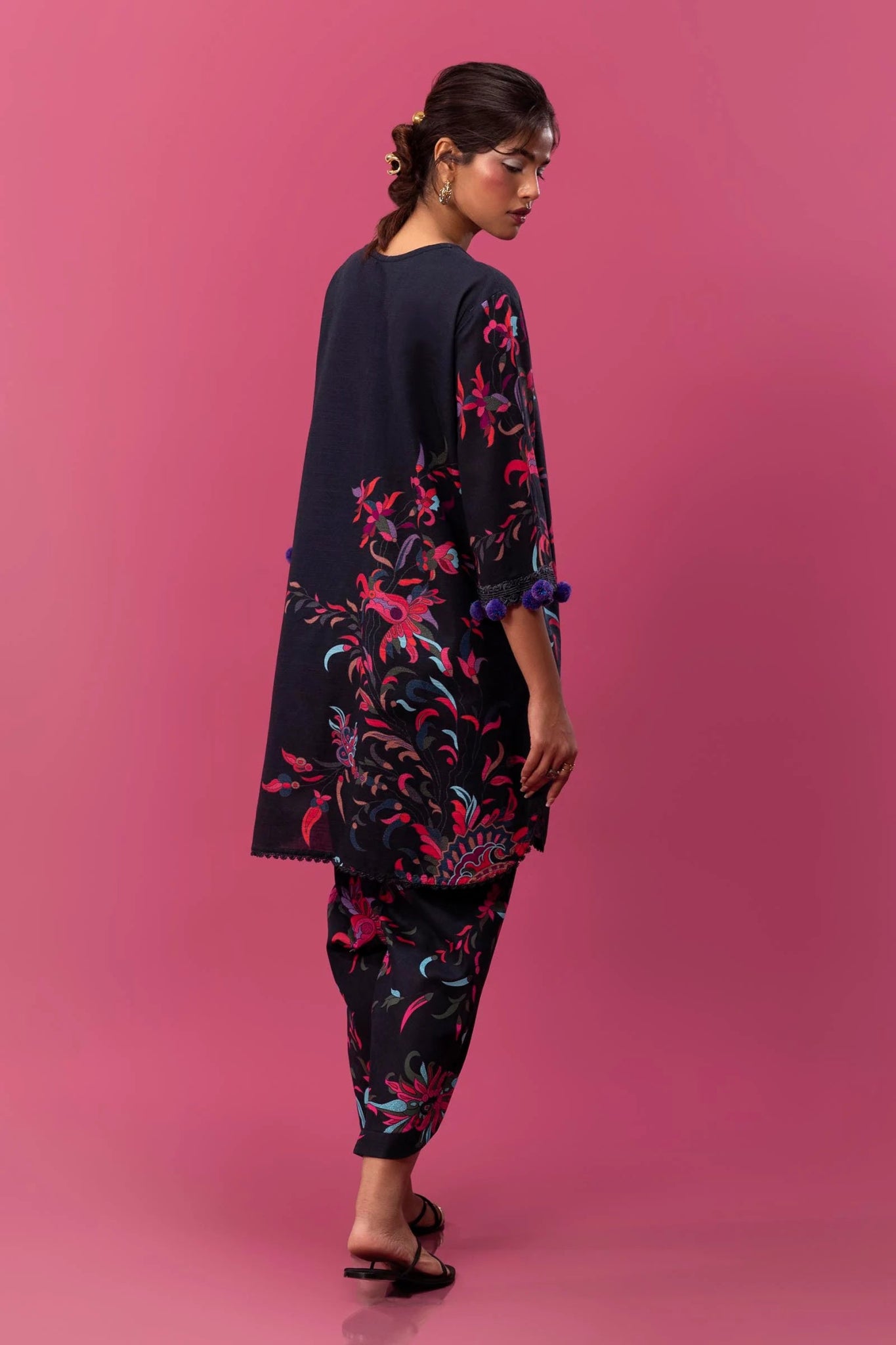 Model wearing a two - piece Sana Safinaz outfit from the Mahay Winter '24 collection, featuring a digitally printed slub shirt with vibrant floral motifs and embroidered details on the sleeves. The ensemble is paired with matching cambric pants, creating a stylish and coordinated look. Available online in the UK.