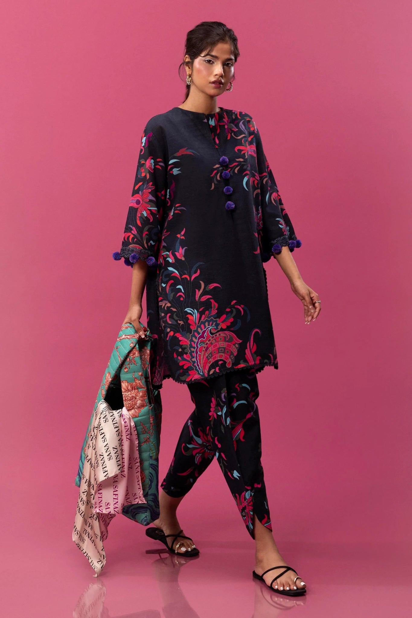 Model wearing a two - piece Sana Safinaz outfit from the Mahay Winter '24 collection, featuring a digitally printed slub shirt with vibrant floral motifs and embroidered details on the sleeves. The ensemble is paired with matching cambric pants, creating a stylish and coordinated look. Available online in the UK.